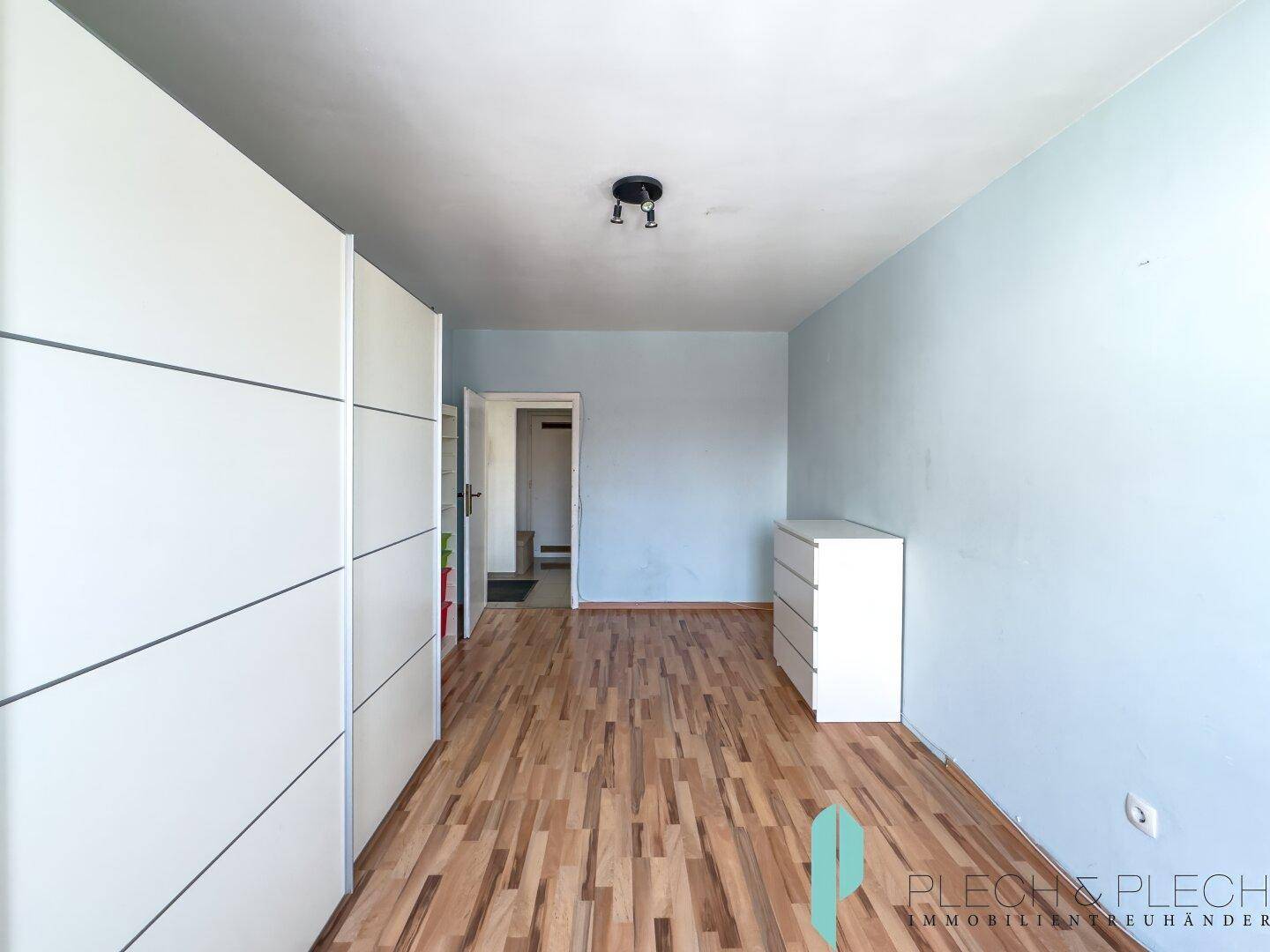 Schlafzimmer mit hellem Laminatboden, blauen Wänden und weißen Einbauschränken.