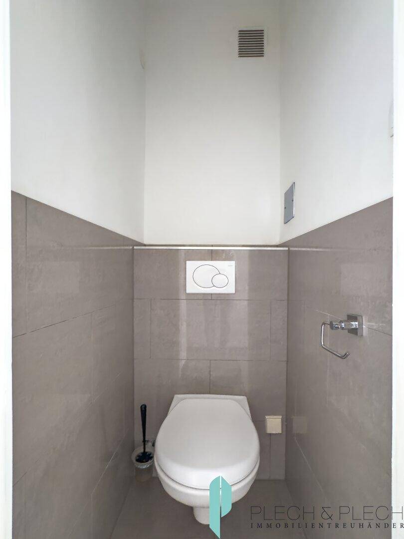 Modernes Gäste-WC mit grauen Fliesen und wandmontierter Toilette.
