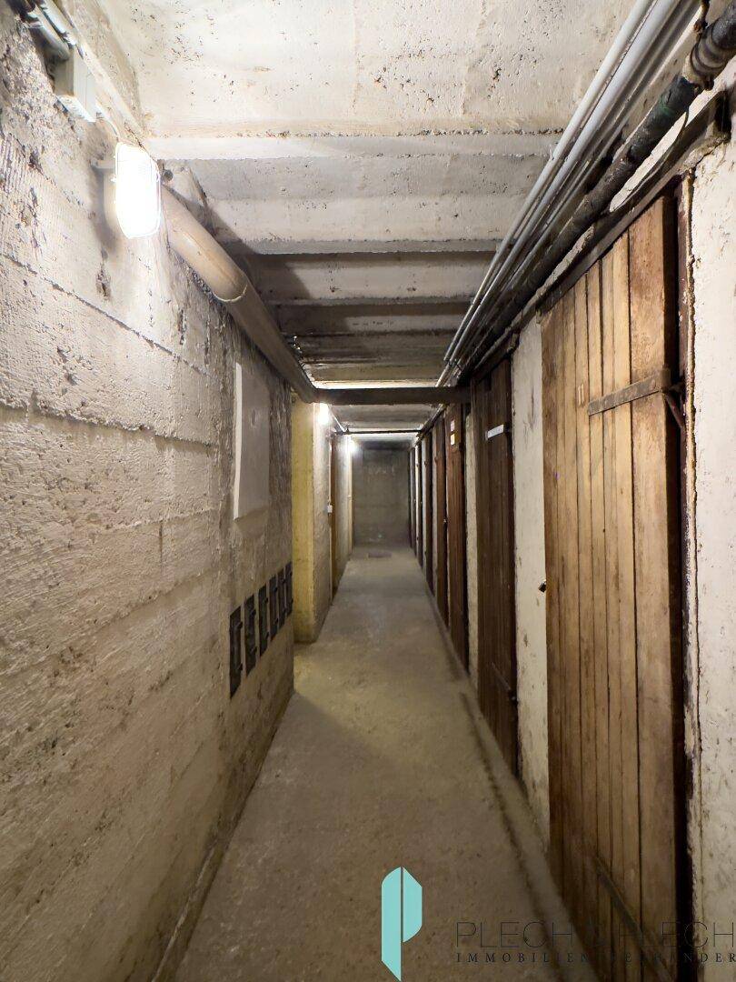 Langer Kellergang mit Betonwänden und Holztüren zu den einzelnen Abteilen.