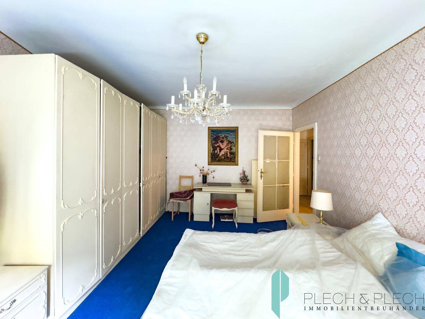 Schlafzimmer mit großem Kleiderschrank, blauem Teppichboden und klassischem Kronleuchter.