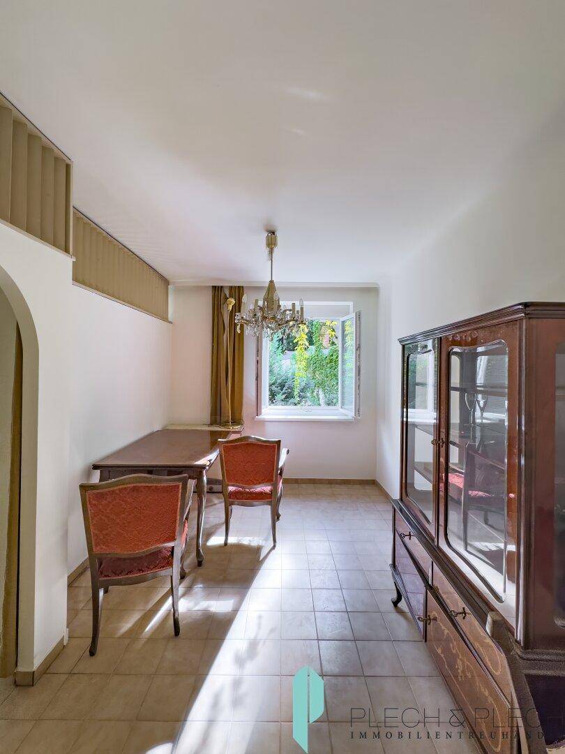Helles Esszimmer mit Fliesenboden, Kronleuchter und Blick auf den Garten.