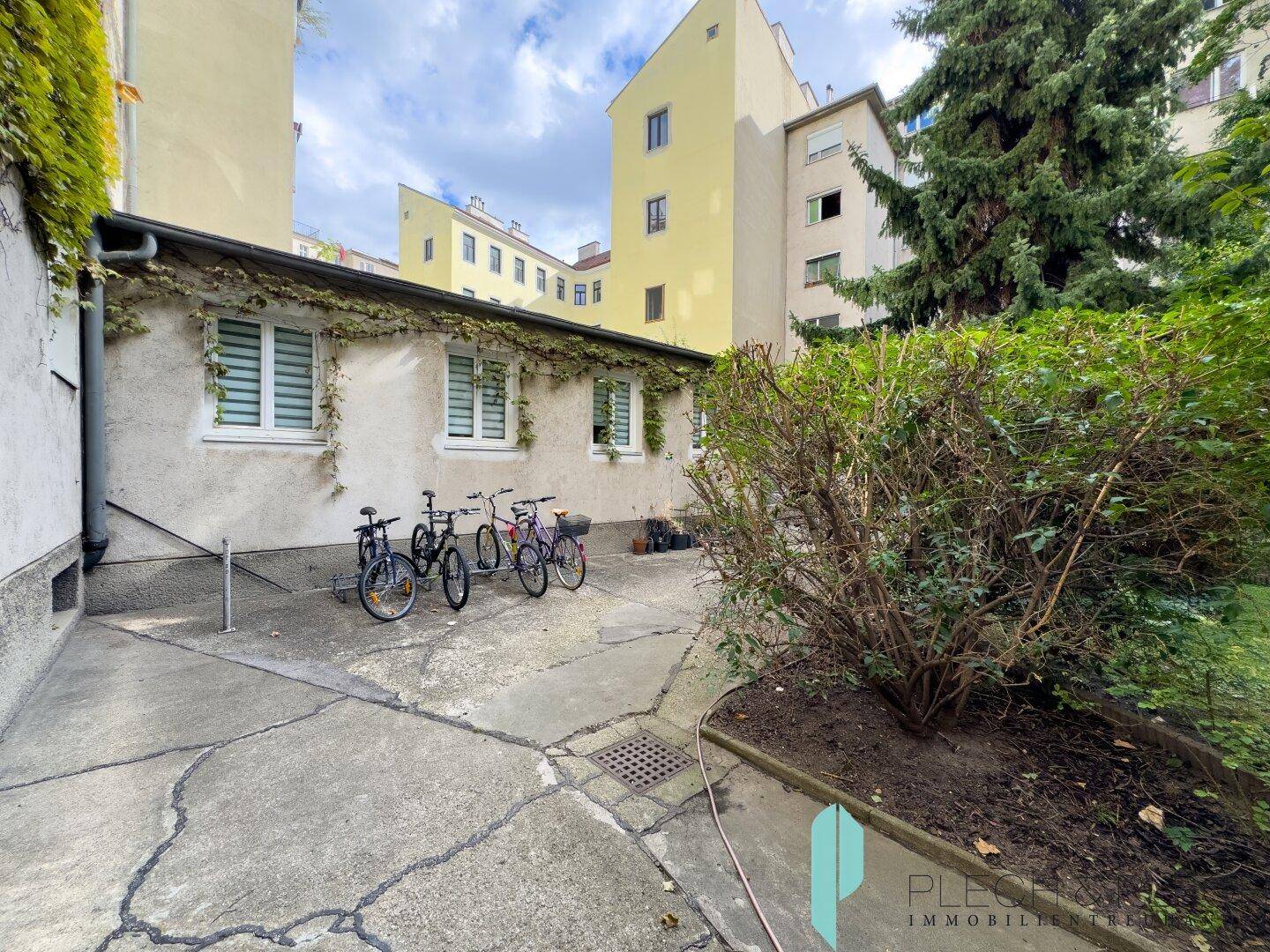 Hinterhof mit Fahrradabstellplatz, Grünflächen und Gebäudefassade.