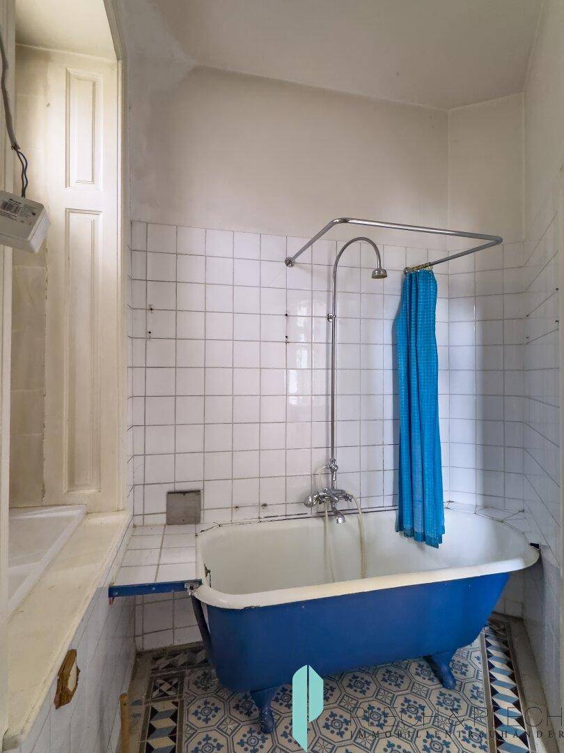 Badezimmer mit freistehender blauer Badewanne, Duschvorhang und weißen Wandfliesen.