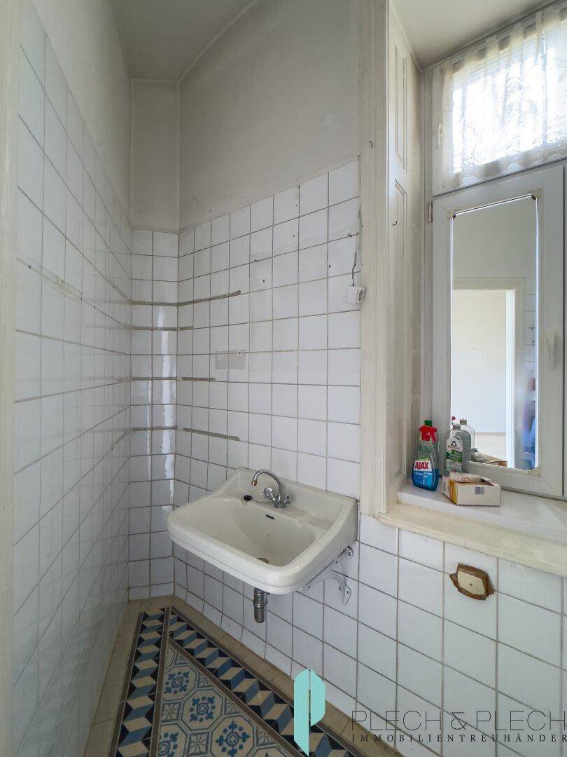 Badezimmer mit Waschbecken, weißen Wandfliesen und einem Fenster für natürliche Belüftung.