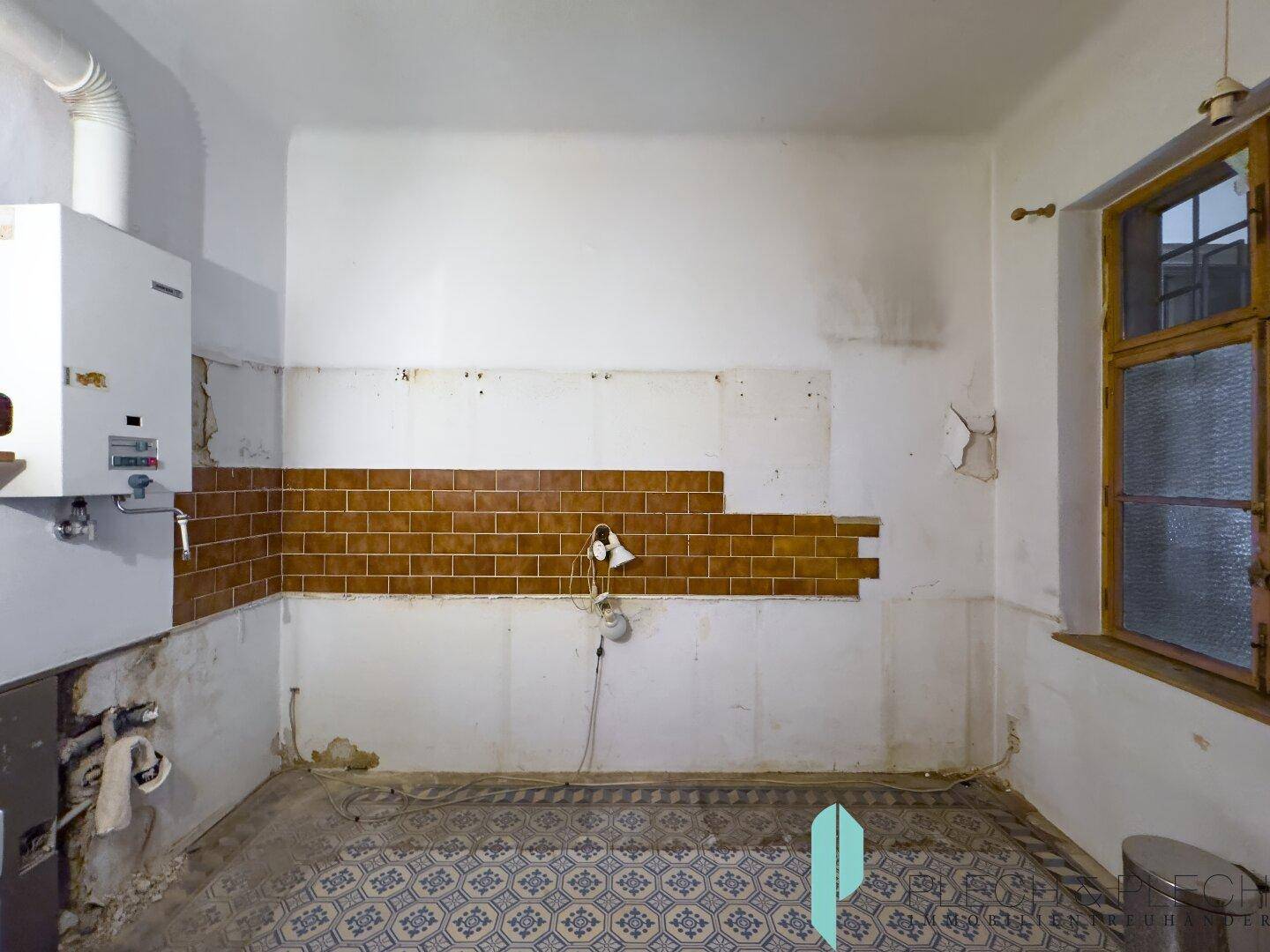 Renovierungsbedürftige Küche mit Fliesenboden, Wandfliesen und einem Fenster für Tageslicht.