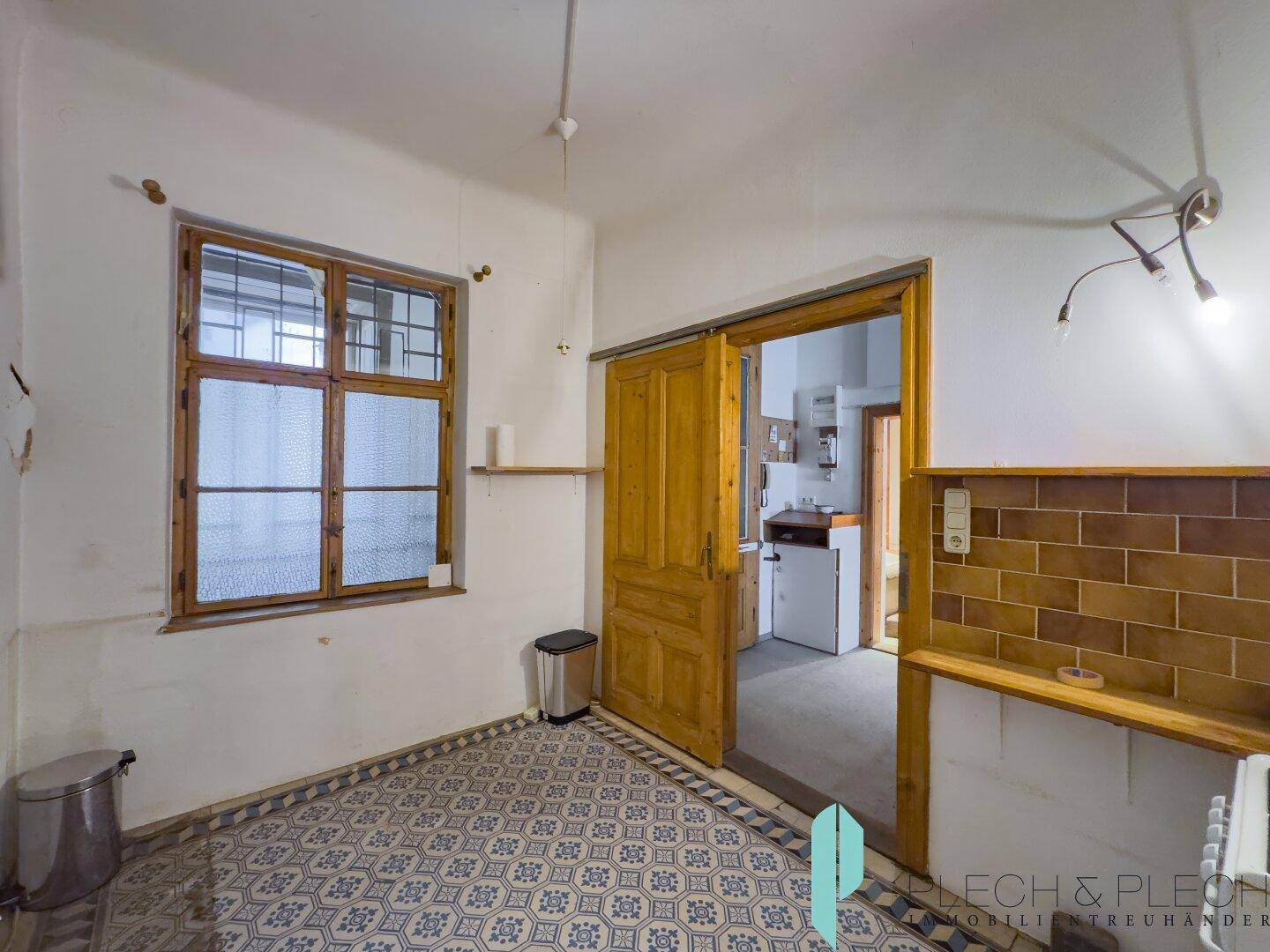 Küche mit gemustertem Fliesenboden, Holzfenster und Schiebetür zu einem weiteren Raum.