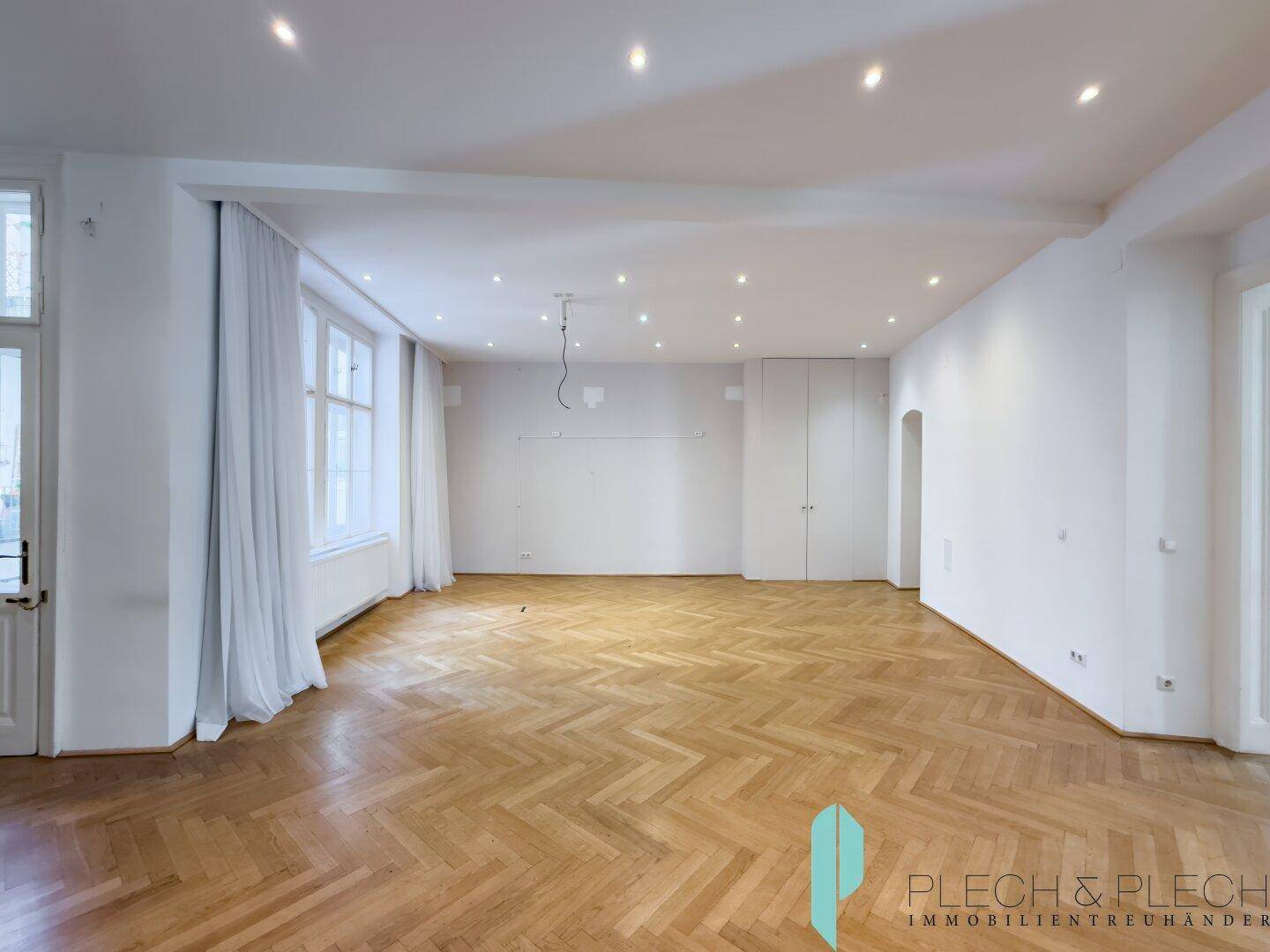 Heller Raum mit Fischgrätparkett, hohen Fenstern und integrierten Schränken an der Wand.