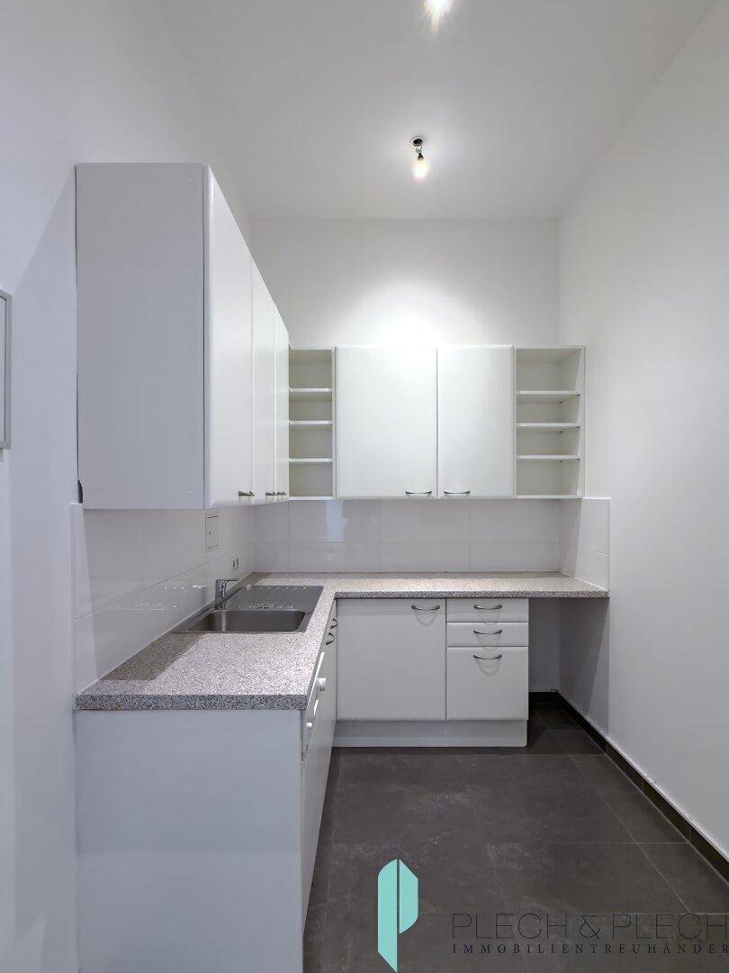 Funktionale Küchenzeile mit weißen Schränken, Granitarbeitsplatte und dunklem Fliesenboden.