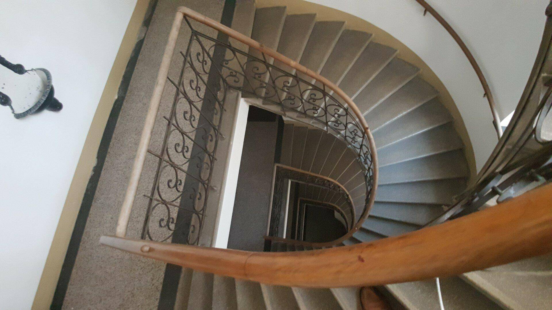 Elegantes Treppenhaus mit geschwungener Wendeltreppe, schmiedeeisernem Geländer und Holzhandlauf.