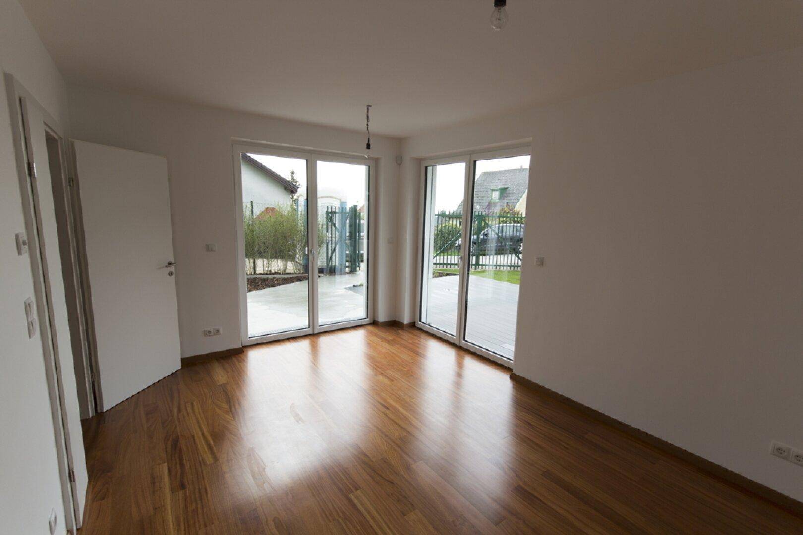 Geräumiges Zimmer mit glänzendem Holzboden und Eckfenstern, die viel Tageslicht hereinlassen.
