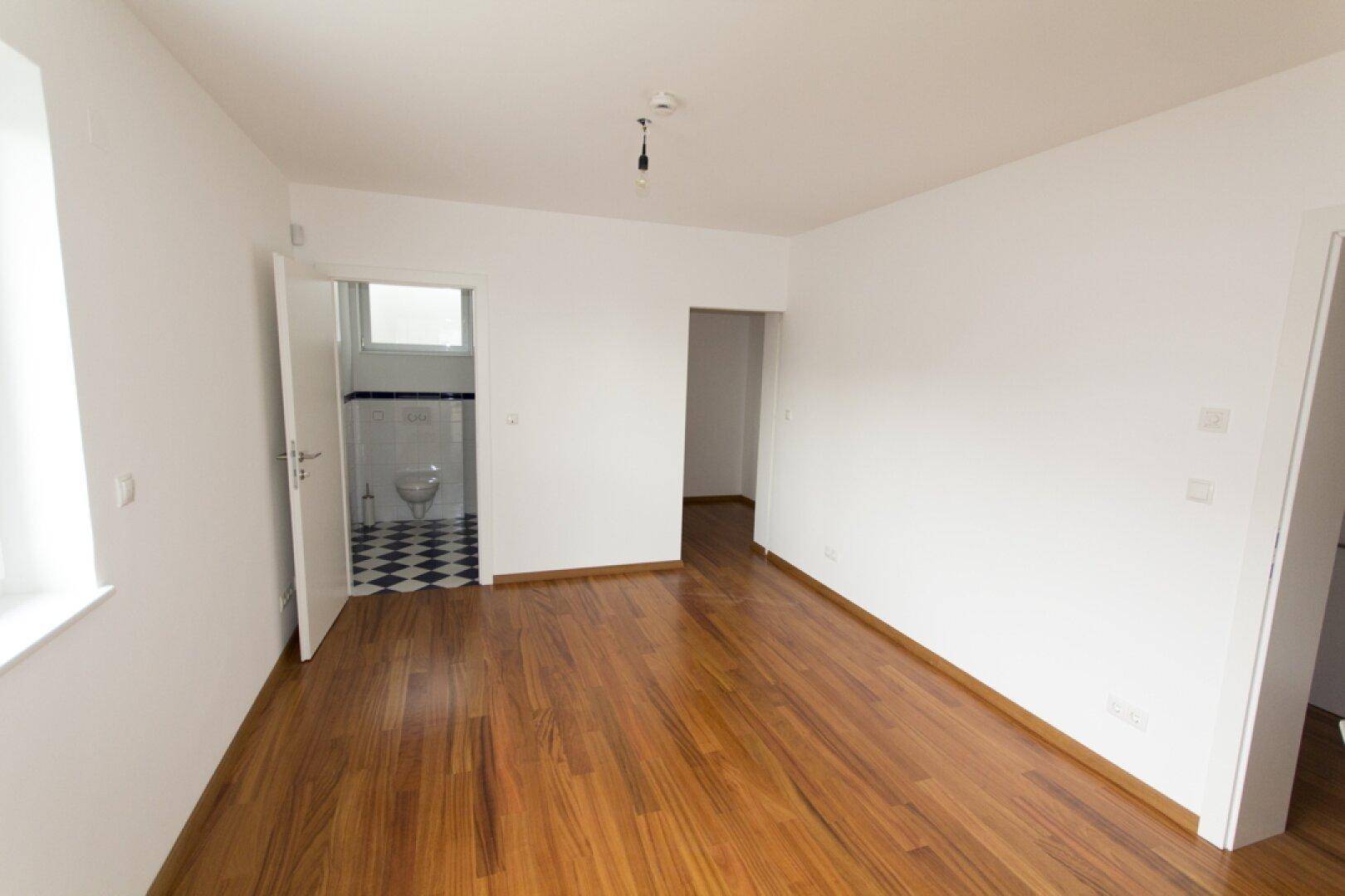 Helles Zimmer mit Holzboden und direktem Zugang zu einem Badezimmer mit markanten Fliesen.