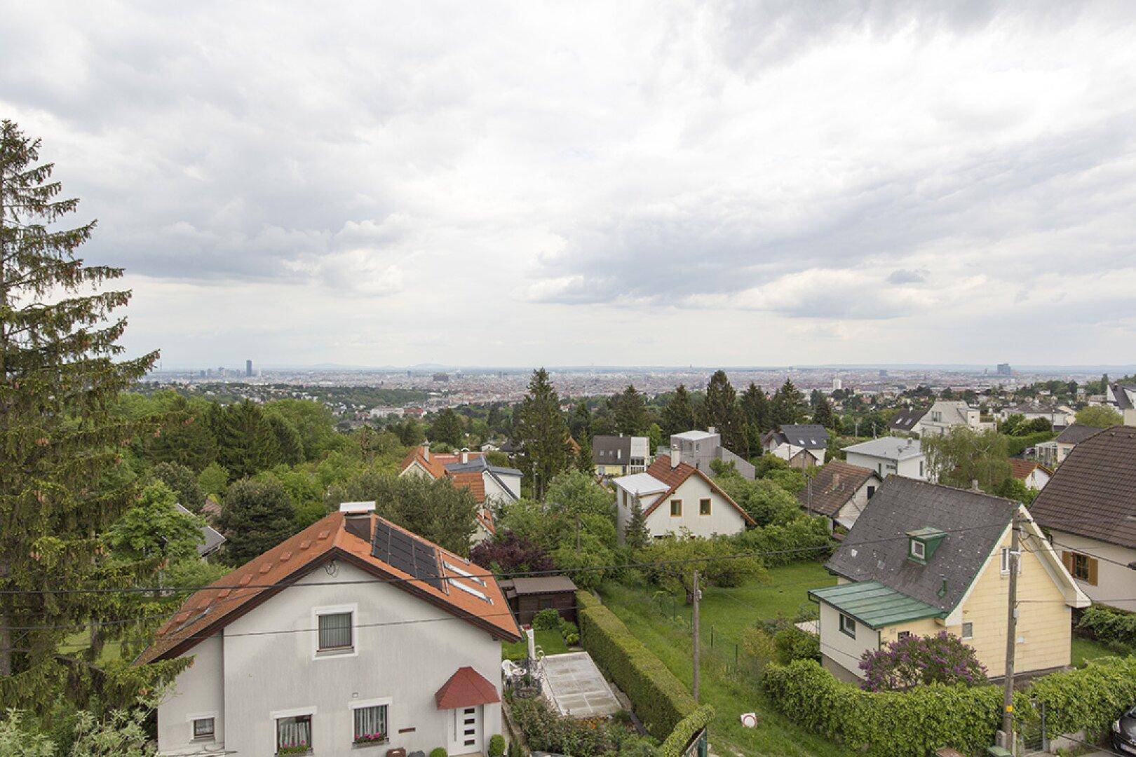 Weitläufiger Blick über eine Wohnsiedlung mit viel Grün und der Stadt im Hintergrund.