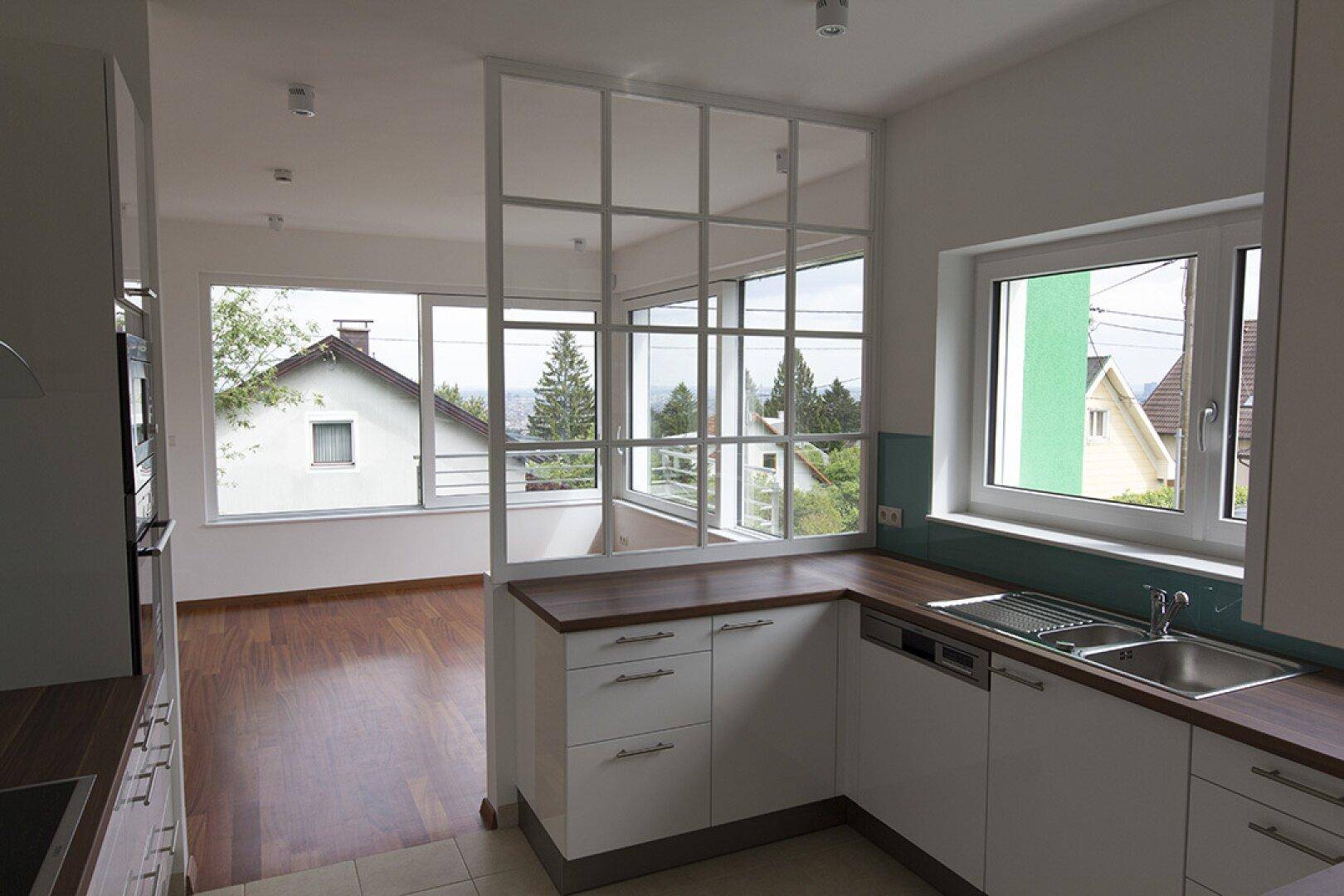 Helle Einbauküche mit weißen Schränken, Holzarbeitsplatte und Blick in den angrenzenden Wohnbereich.