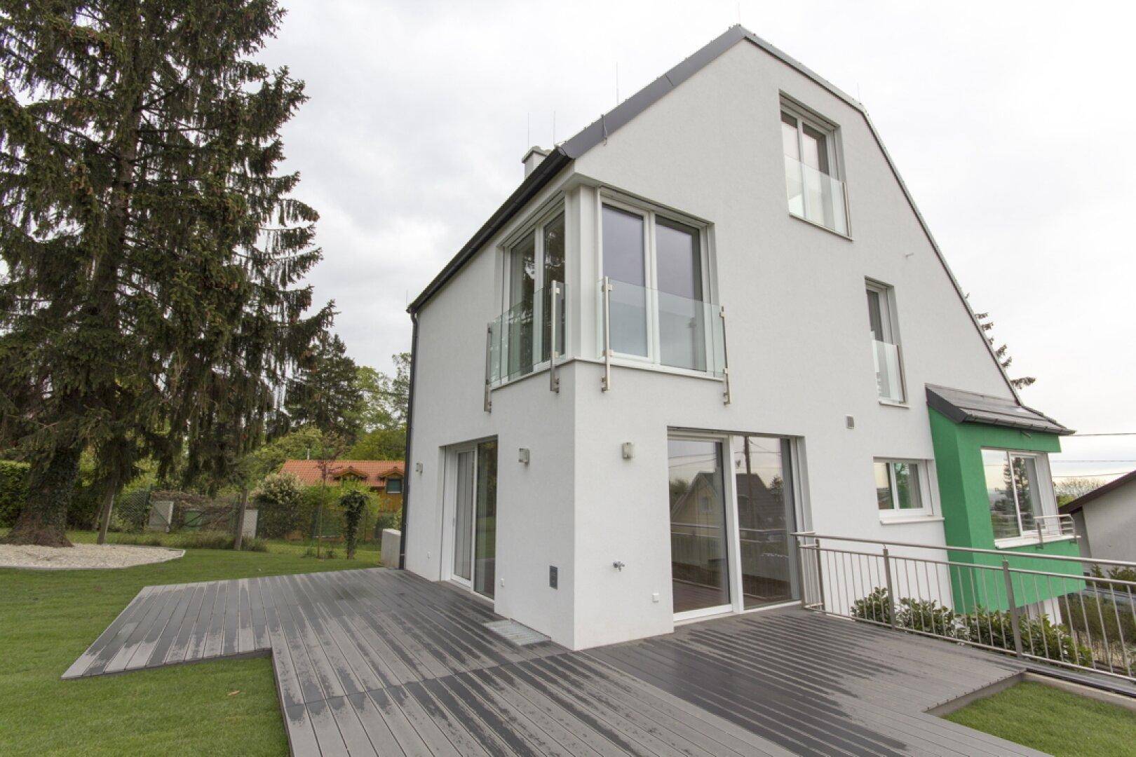 Große Holzterrasse am Haus, umgeben von Grünflächen und einem alten Baum.