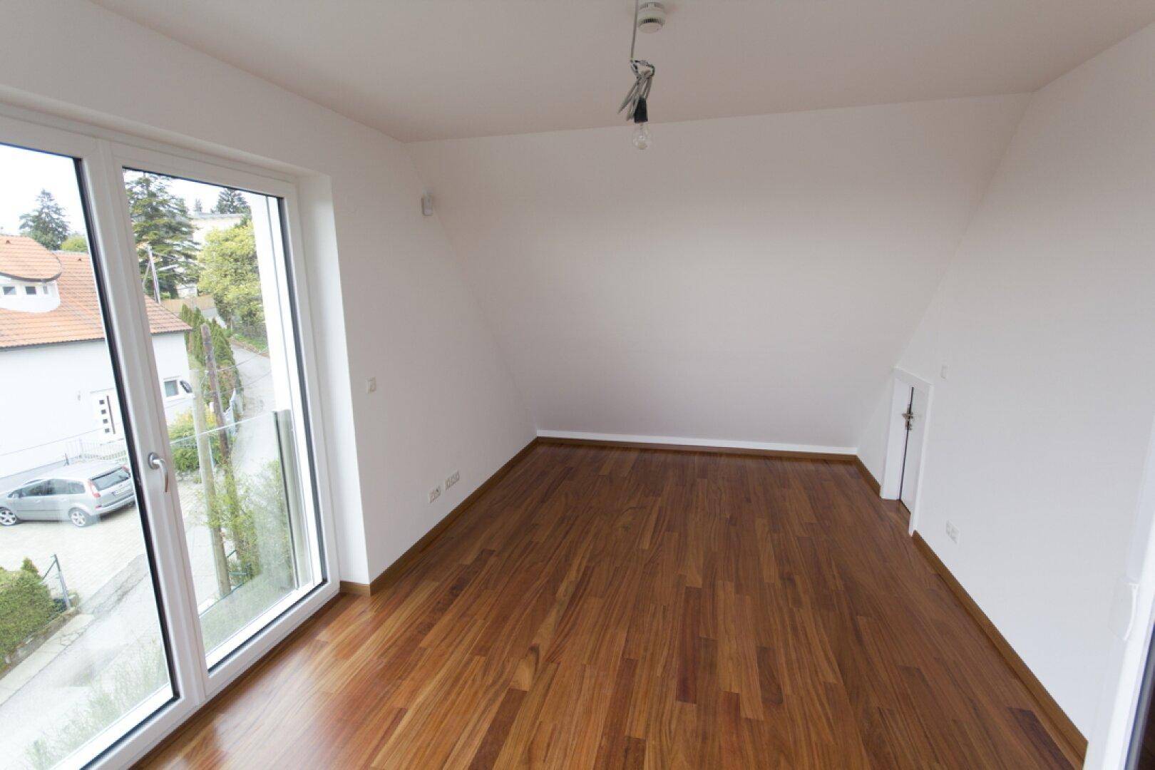 Helles Dachgeschosszimmer mit Holzboden und schräger Decke, bietet einen schönen Ausblick.