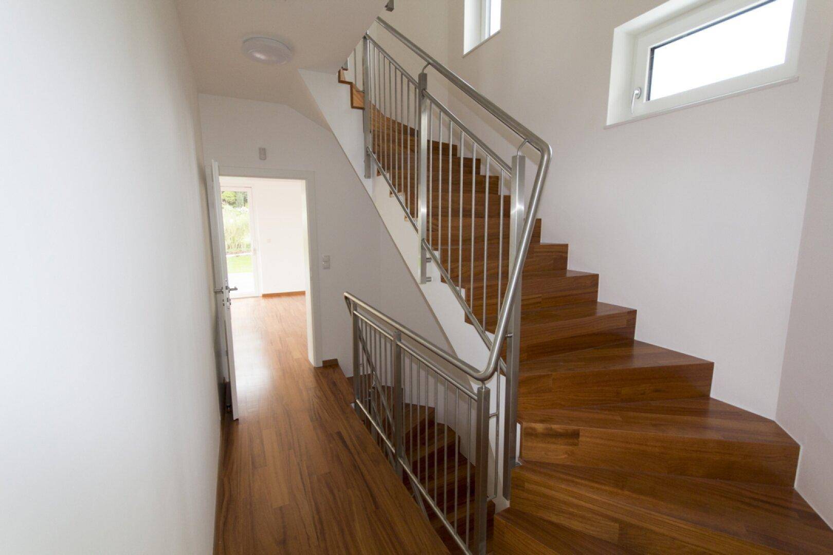 Moderner Flur mit Holztreppe und elegantem Edelstahlgeländer, der die Stockwerke verbindet.