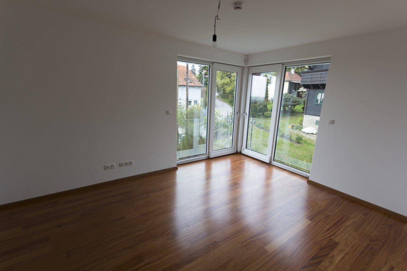 Helles Zimmer mit Holzboden und großen Glastüren, die Zugang zu einem Außenbereich bieten.