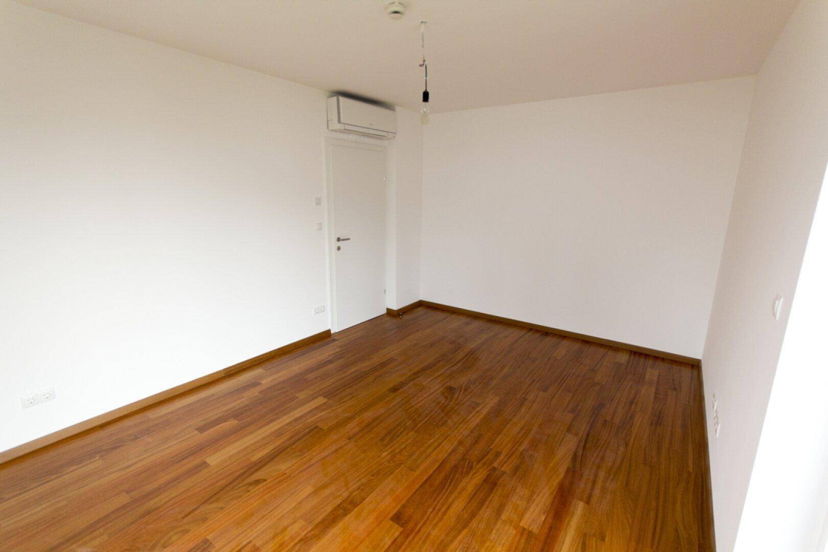 Geräumiges Zimmer mit Holzboden und installierter Klimaanlage für angenehmes Raumklima.