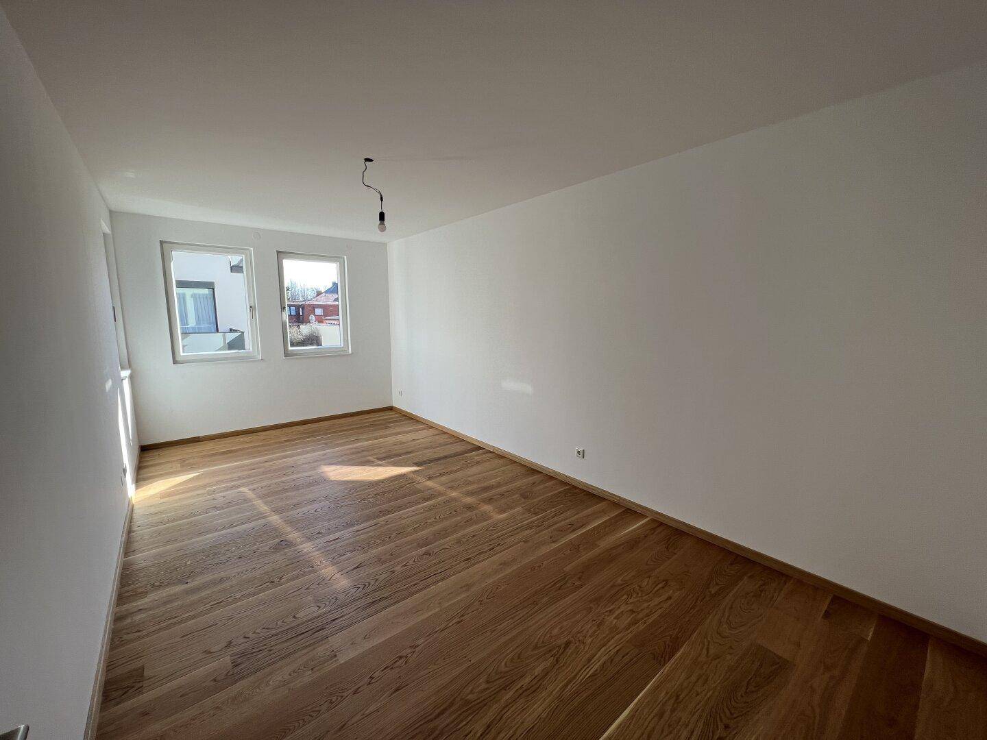 Helles Schlafzimmer mit Holzboden und zwei Fenstern, bereit zur individuellen Gestaltung.