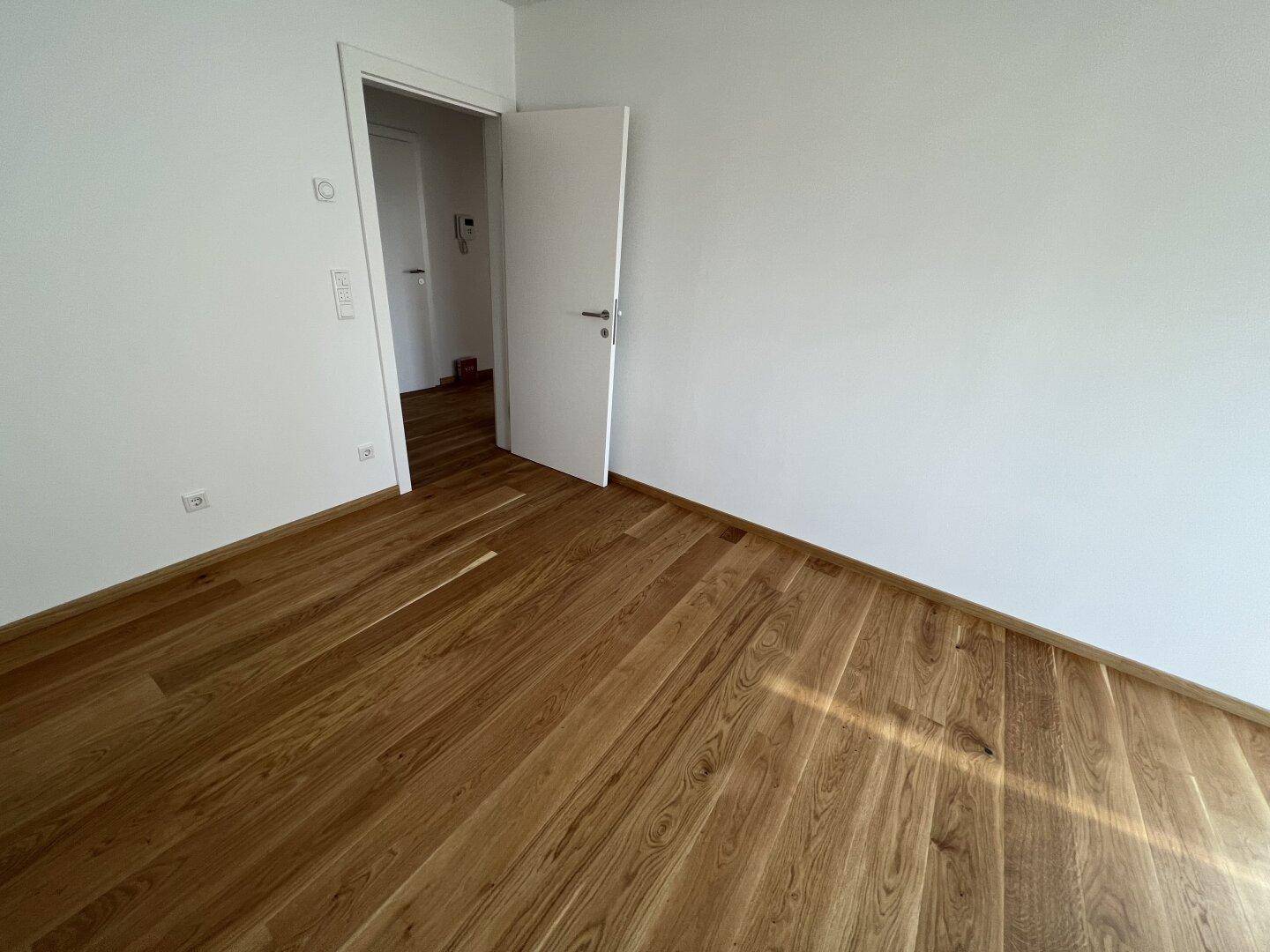 Leeres Zimmer mit Holzboden und weiß gestrichenen Wänden, bereit für neue Bewohner.