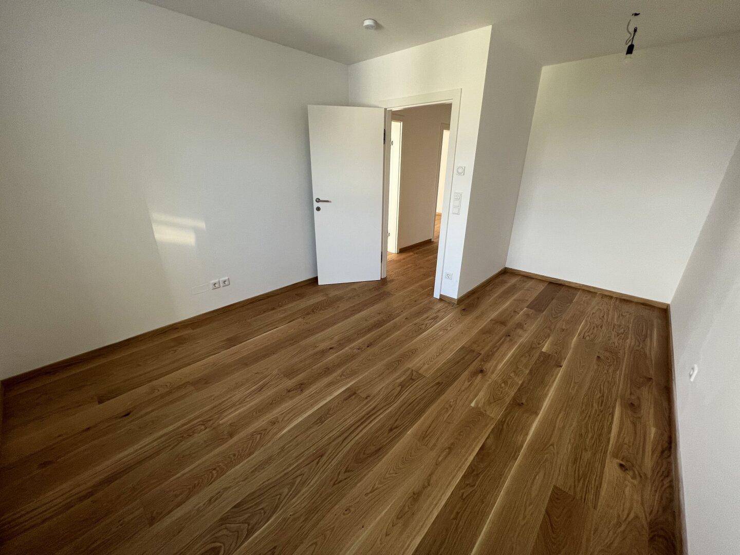 Leeres Zimmer mit Holzboden und weiß gestrichenen Wänden, bereit zur individuellen Einrichtung.