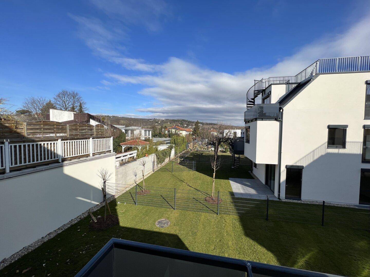 Gepflegter Gartenbereich mit Rasen und junger Bepflanzung hinter einem modernen Wohngebäude.