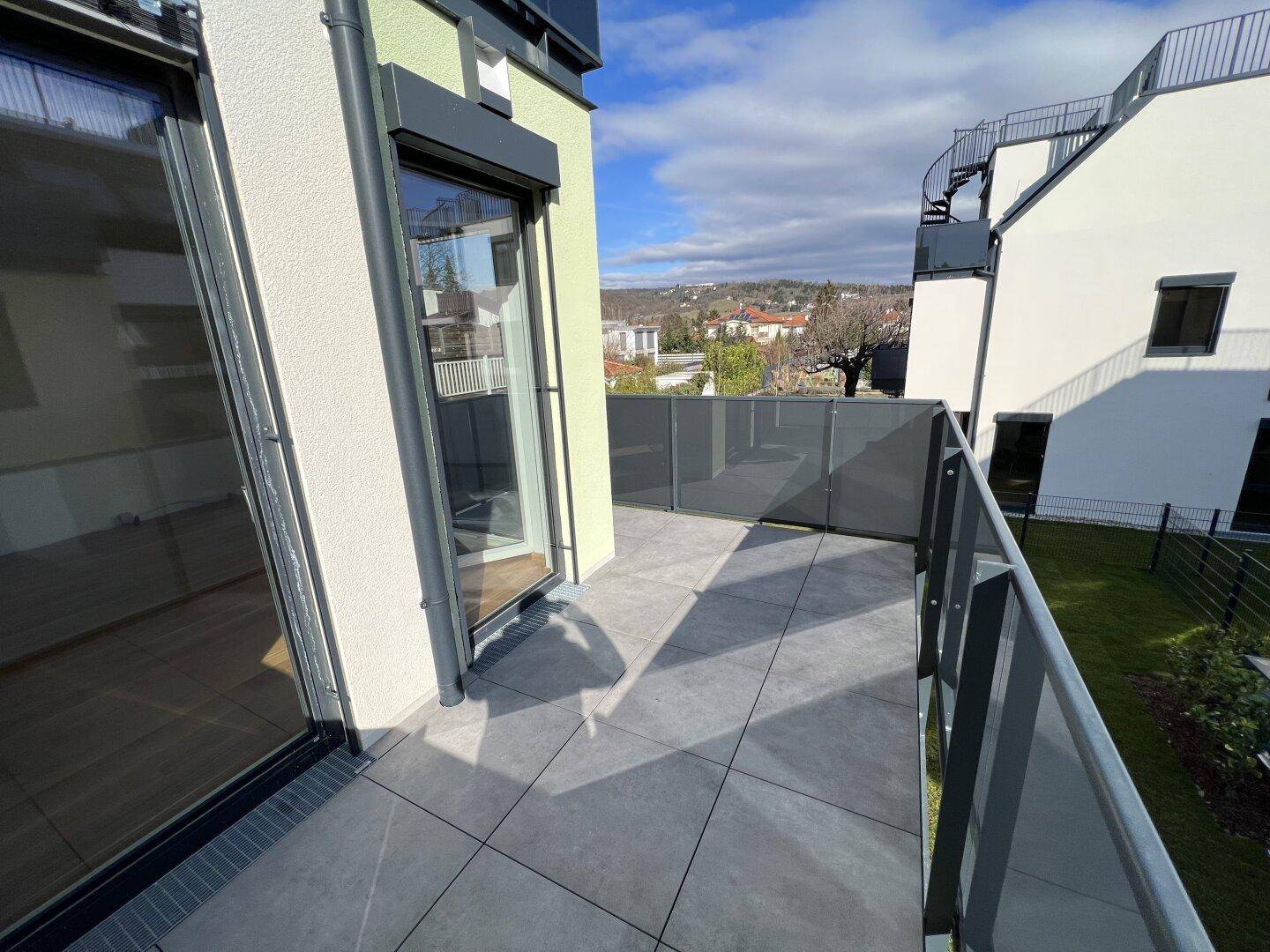 Geräumiger Balkon mit grauen Fliesen und blickdichter Brüstung, ideal für Privatsphäre.
