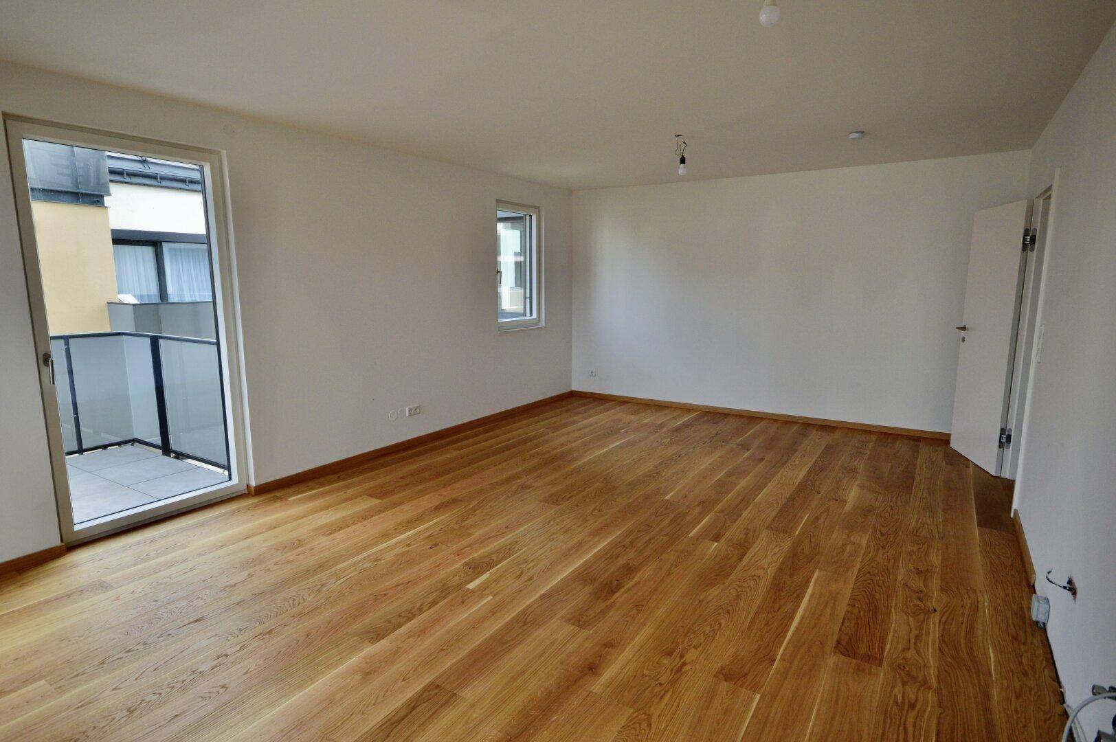 Geräumiger, heller Raum mit Holzboden und direktem Zugang zu einem Balkon.