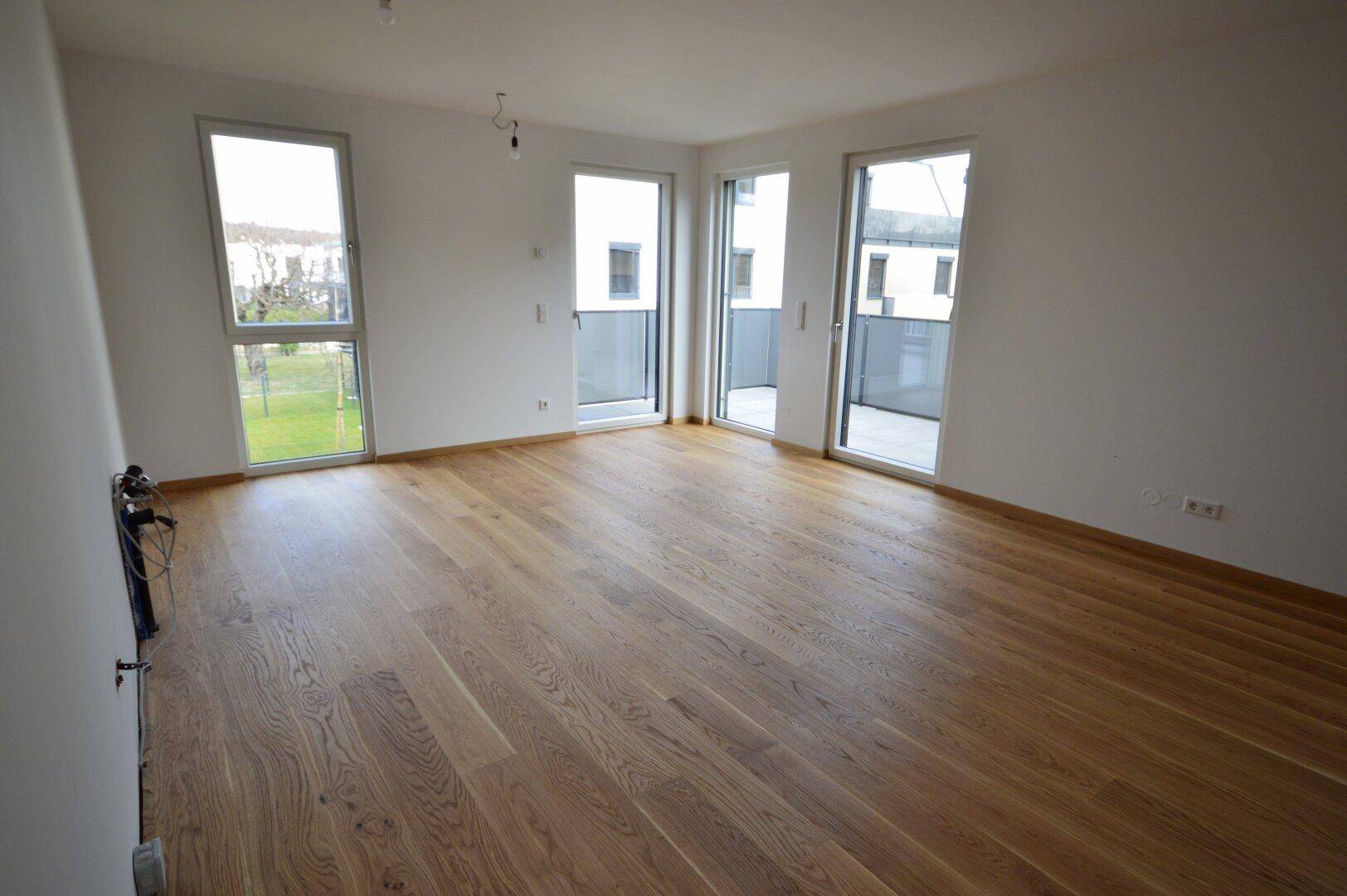 Heller, leerer Wohnraum mit Eichenparkettboden und Zugang zu mehreren Balkonen.