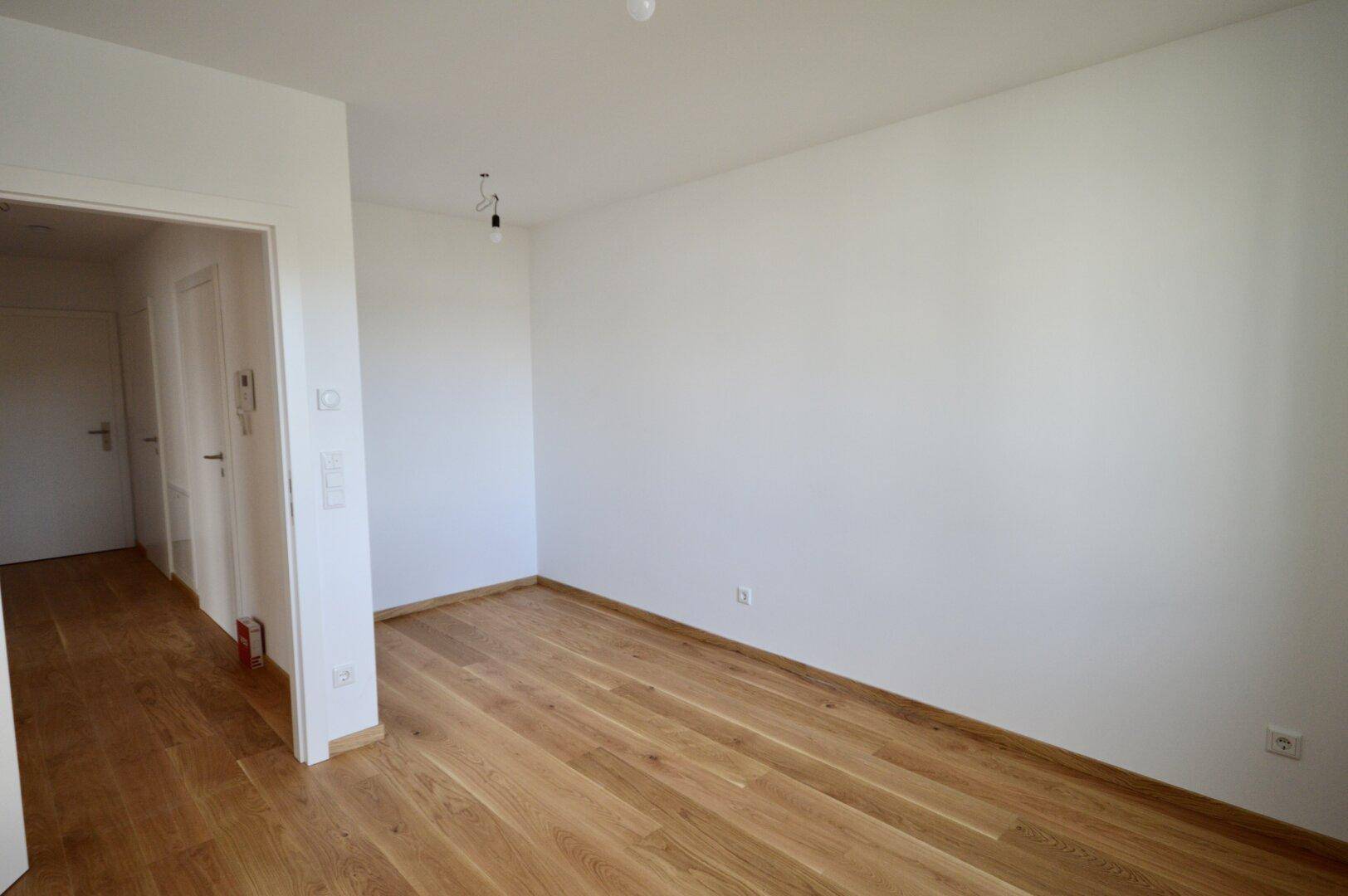 Heller Raum mit Holzboden und Zugang zum Flur, vielseitig nutzbar als Schlaf- oder Arbeitszimmer.