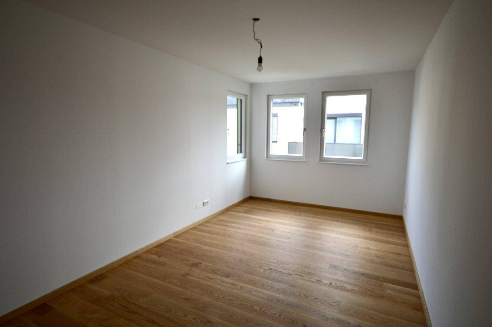 Geräumiges Schlafzimmer mit Holzboden und drei Fenstern, die viel Tageslicht hereinlassen.