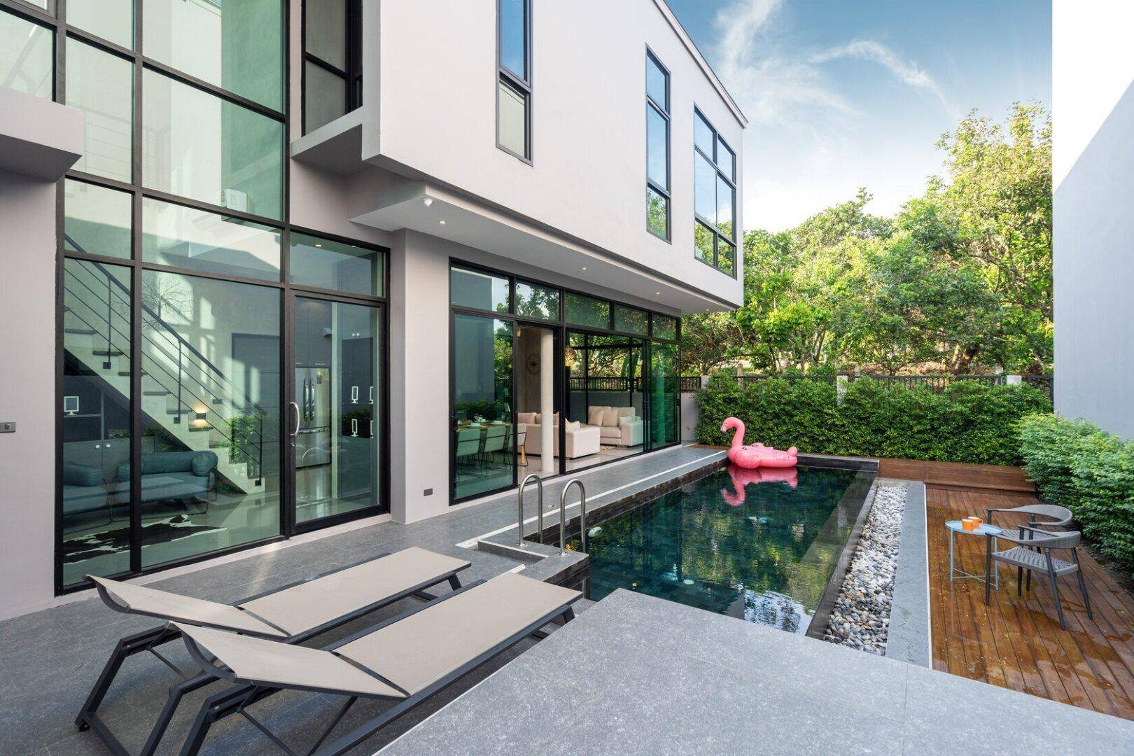Moderne Villa mit großem Pool, Holzdeck und raumhohen Glasfronten im Gartenbereich.
