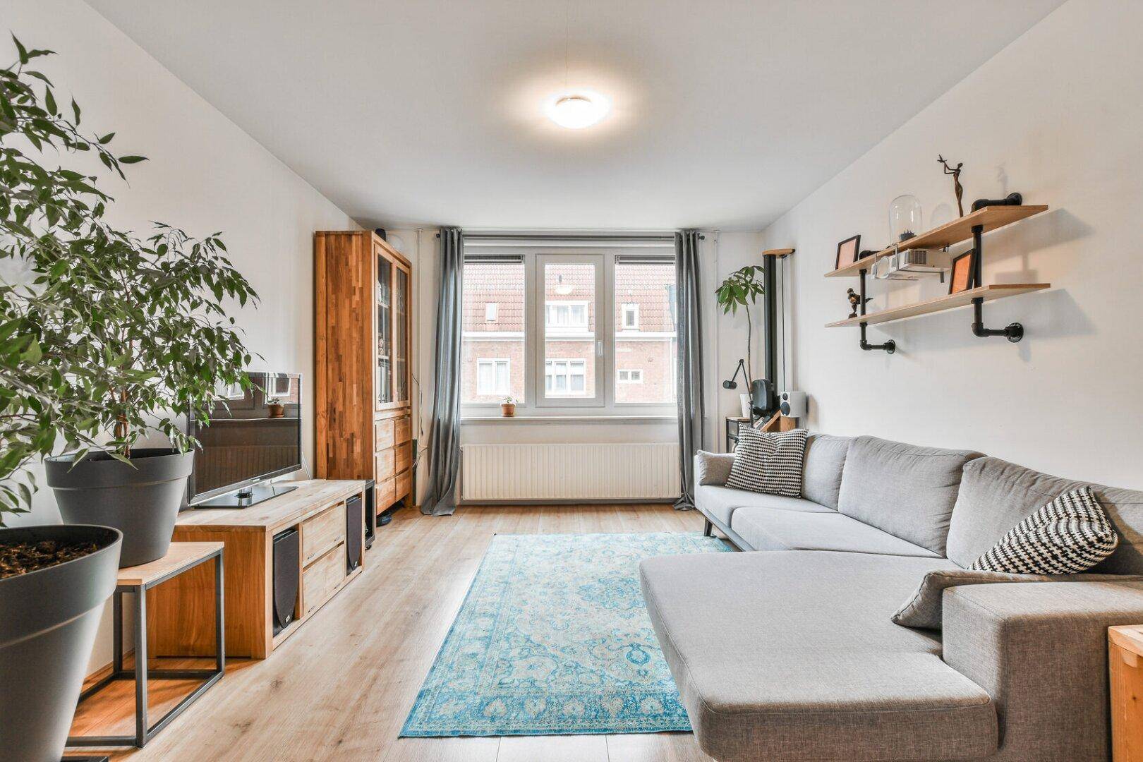 Gemütliches Wohnzimmer mit hellem Holzboden, großem Sofa und dekorativen Pflanzen.