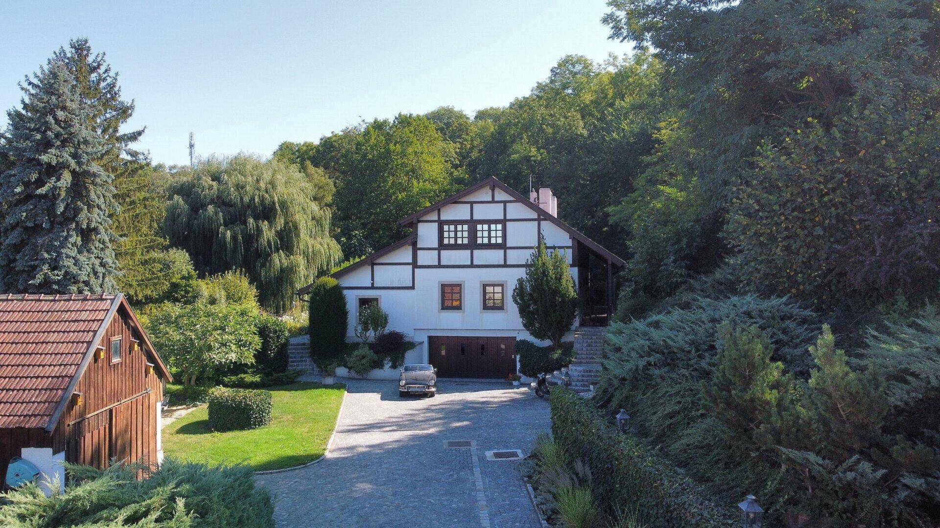 Malerisches Haus mit Fachwerk und Nebengebäude, umgeben von üppiger Natur.