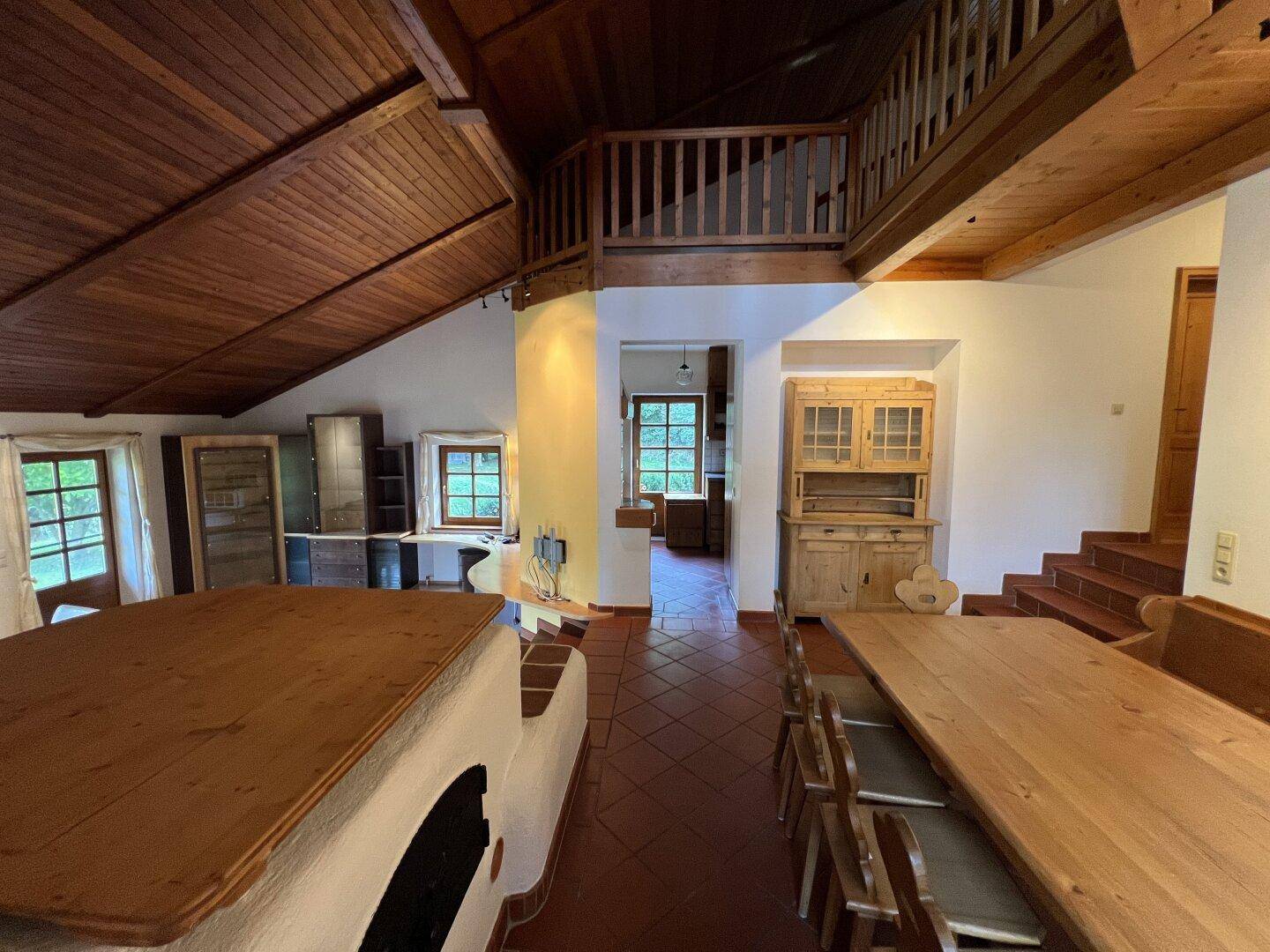 Rustikaler Essbereich mit Holztisch, Kachelofen und Zugang zu einer Galerie.