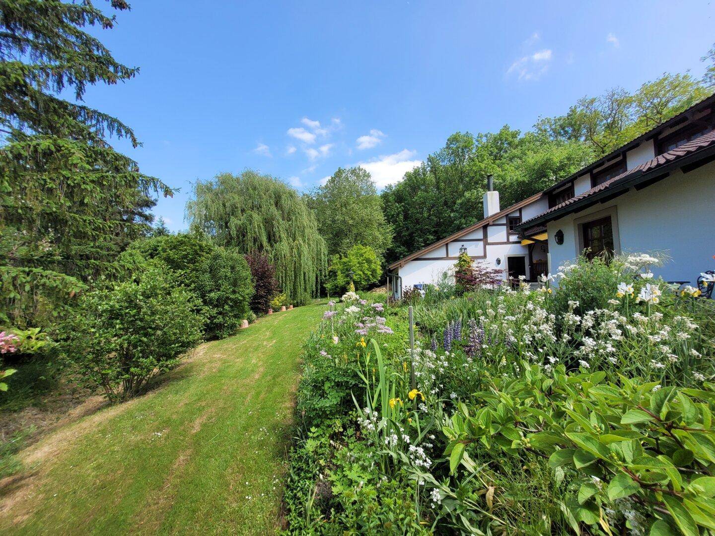 Blühender Garten mit vielfältigen Blumenbeeten und weitem Blick ins Grüne.