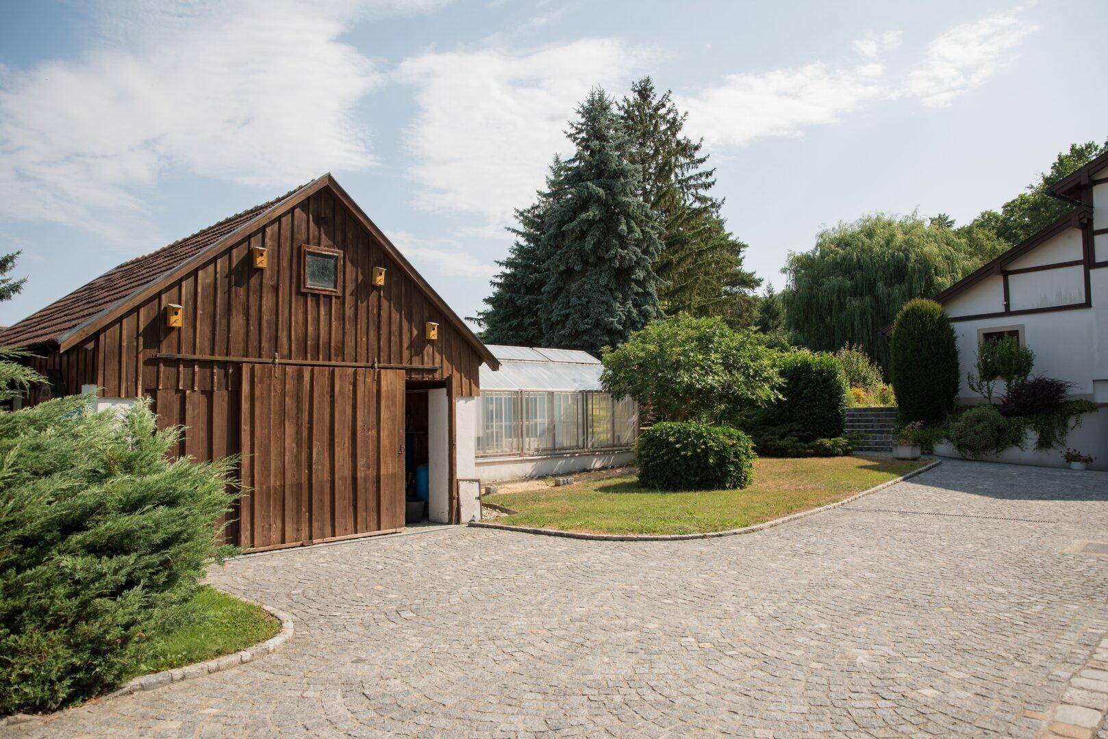 Nebengebäude und Gewächshaus im Gartenbereich, umgeben von Grün.