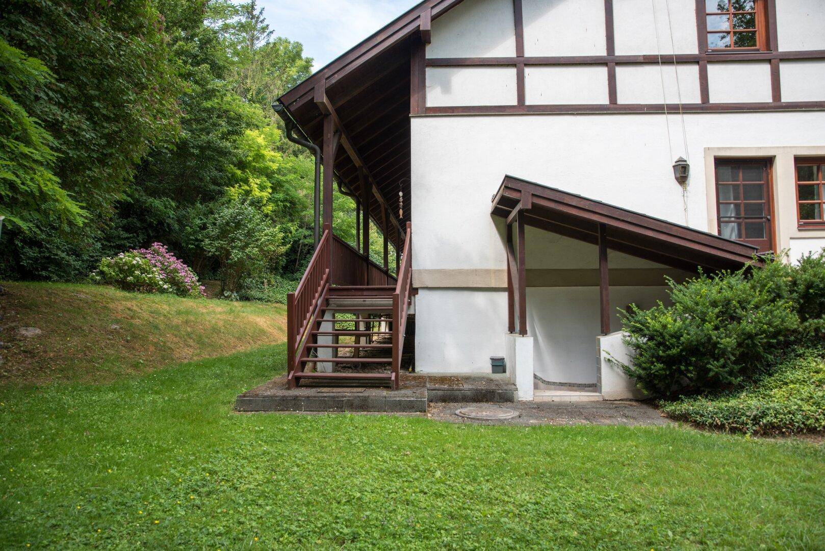 Seitenansicht des Hauses mit Außentreppe und Zugang zu einem überdachten Bereich.