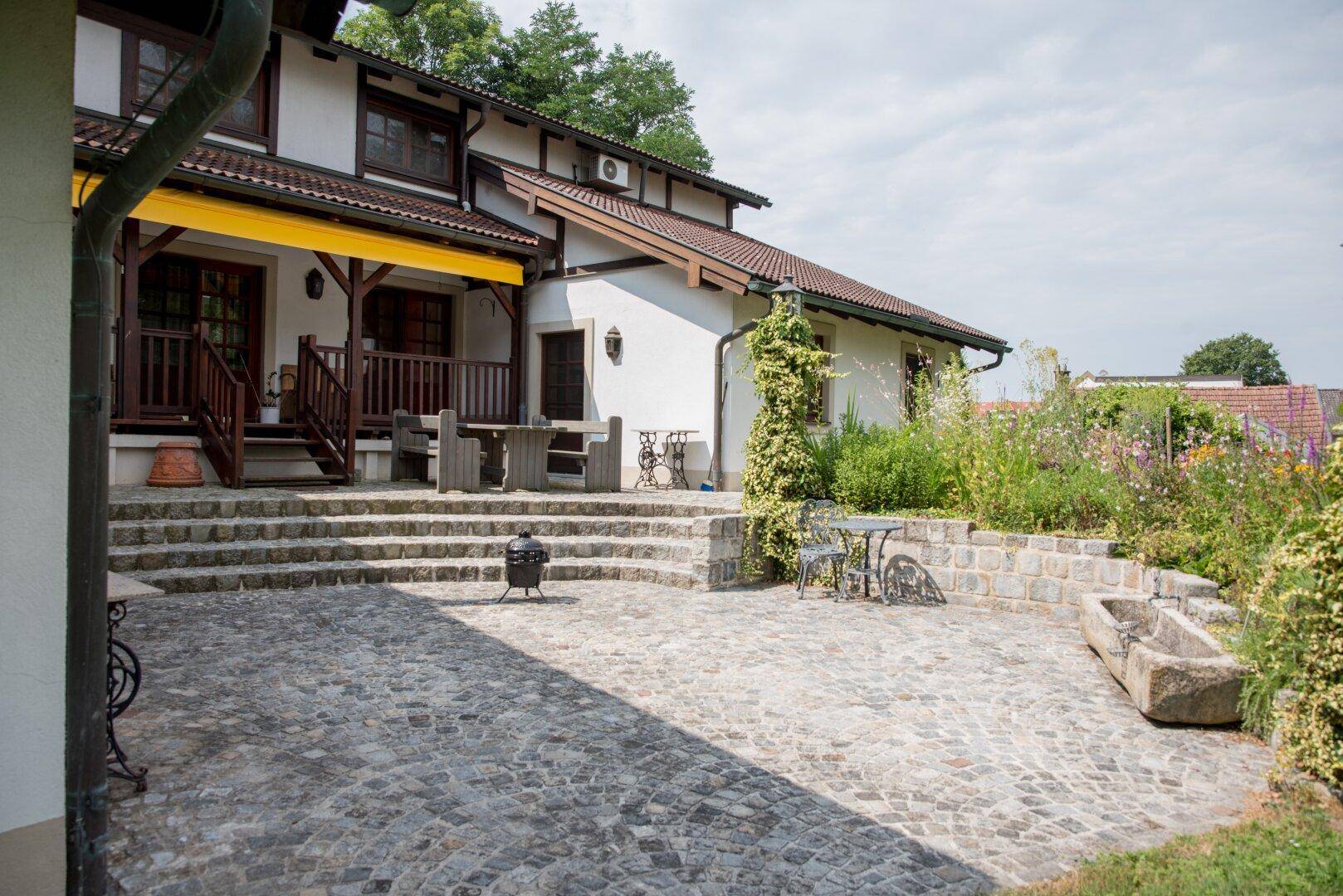 Große gepflasterte Terrasse mit Steinstufen, Sitzgelegenheiten und einer gelben Markise.