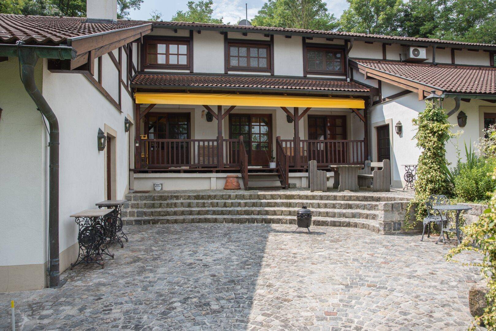 Geräumige Terrasse mit Pflastersteinen, Steinstufen und einer gelben Markise, ideal für Mahlzeiten im Freien.