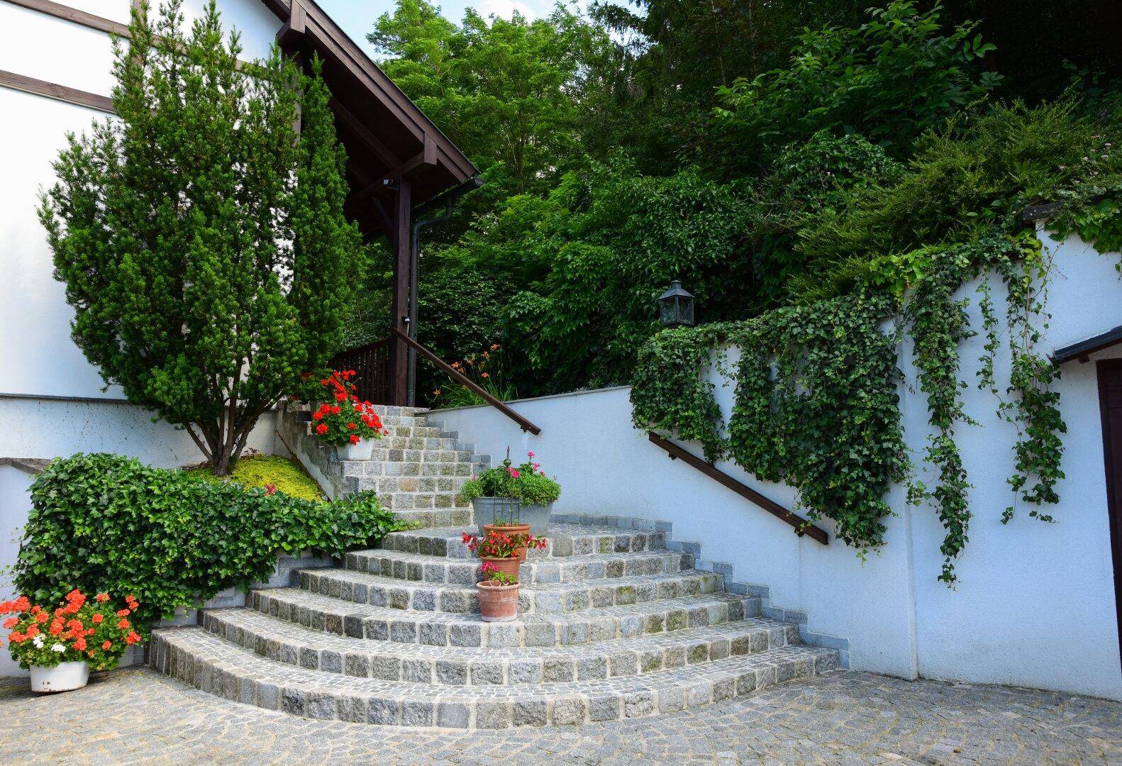 Geschwungene Steintreppe zum Eingang des Hauses, umgeben von üppiger Bepflanzung und Blumen.