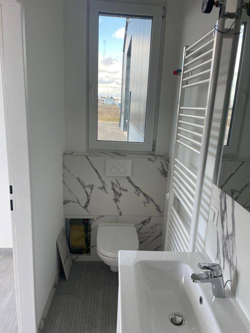 Modernes Badezimmer mit wandhängender Toilette, Waschbecken, Fenster und Fliesen in Marmoroptik.
