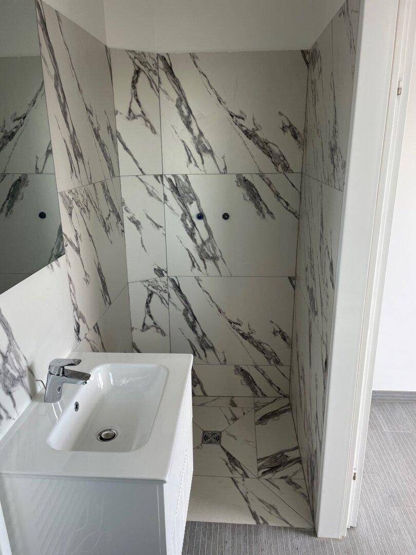 Duschbereich im Badezimmer mit modernen Fliesen in Marmoroptik und einem integrierten Waschbecken.