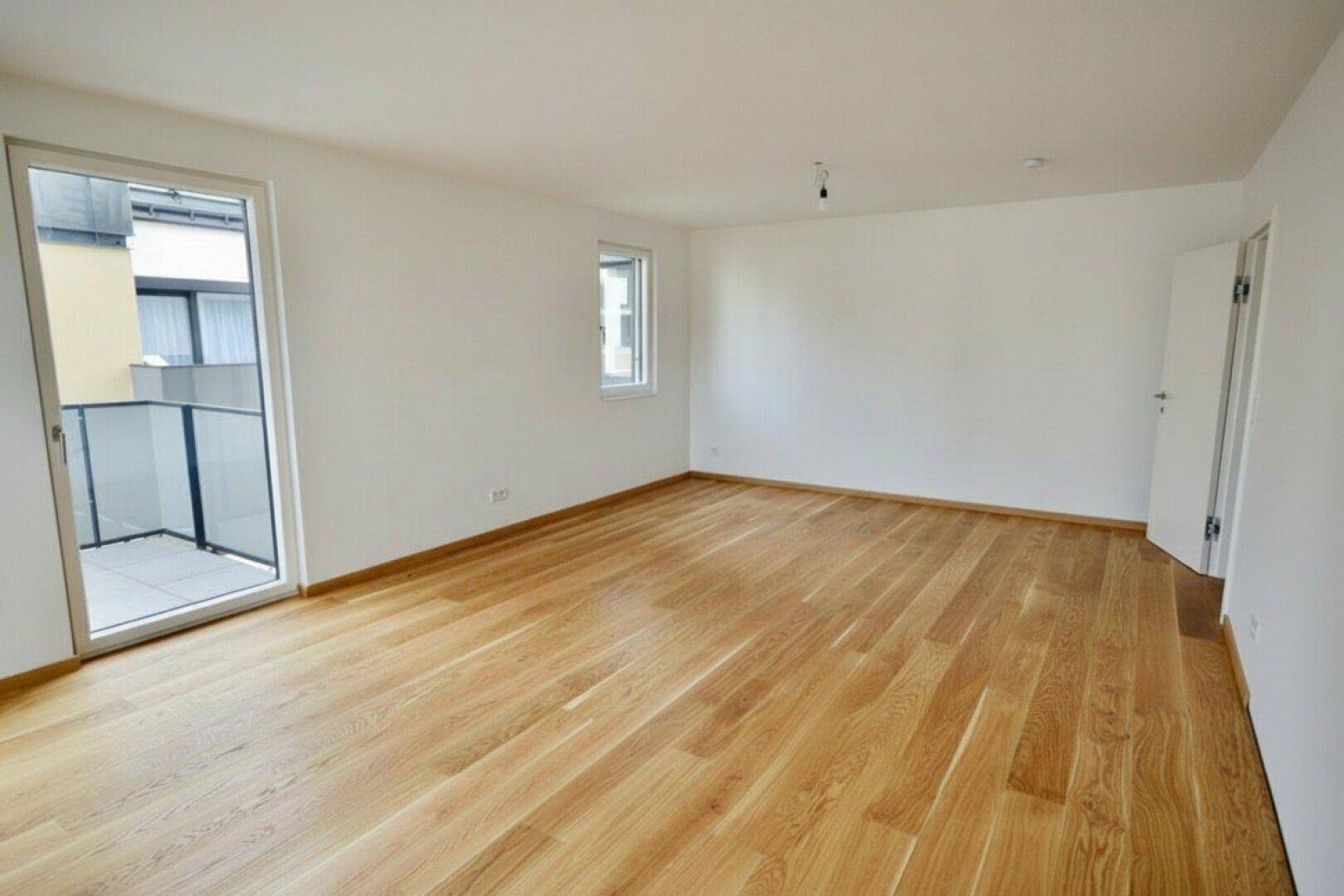 Geräumiges, helles Zimmer mit Holzboden und direktem Zugang zu einem kleinen Balkon.