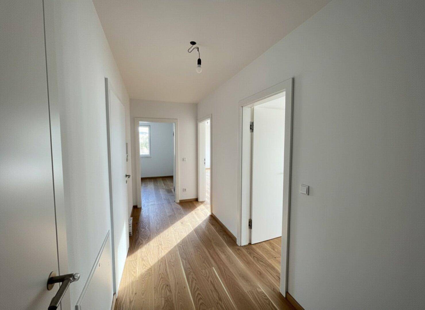 Heller Flur mit Holzboden, der zu verschiedenen Zimmern der Wohnung führt.