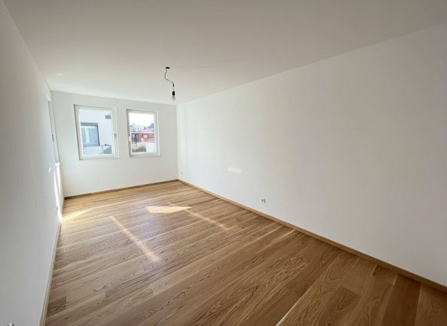 Ruhiges Schlafzimmer mit hellem Parkettboden und zwei Fenstern für viel Tageslicht.