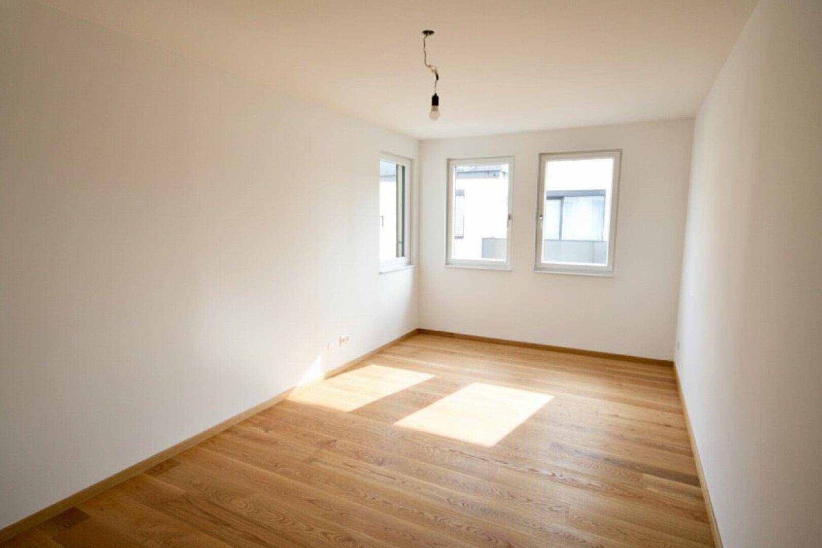 Freundliches Zimmer mit Holzboden und drei Fenstern, ideal als Schlaf- oder Kinderzimmer.