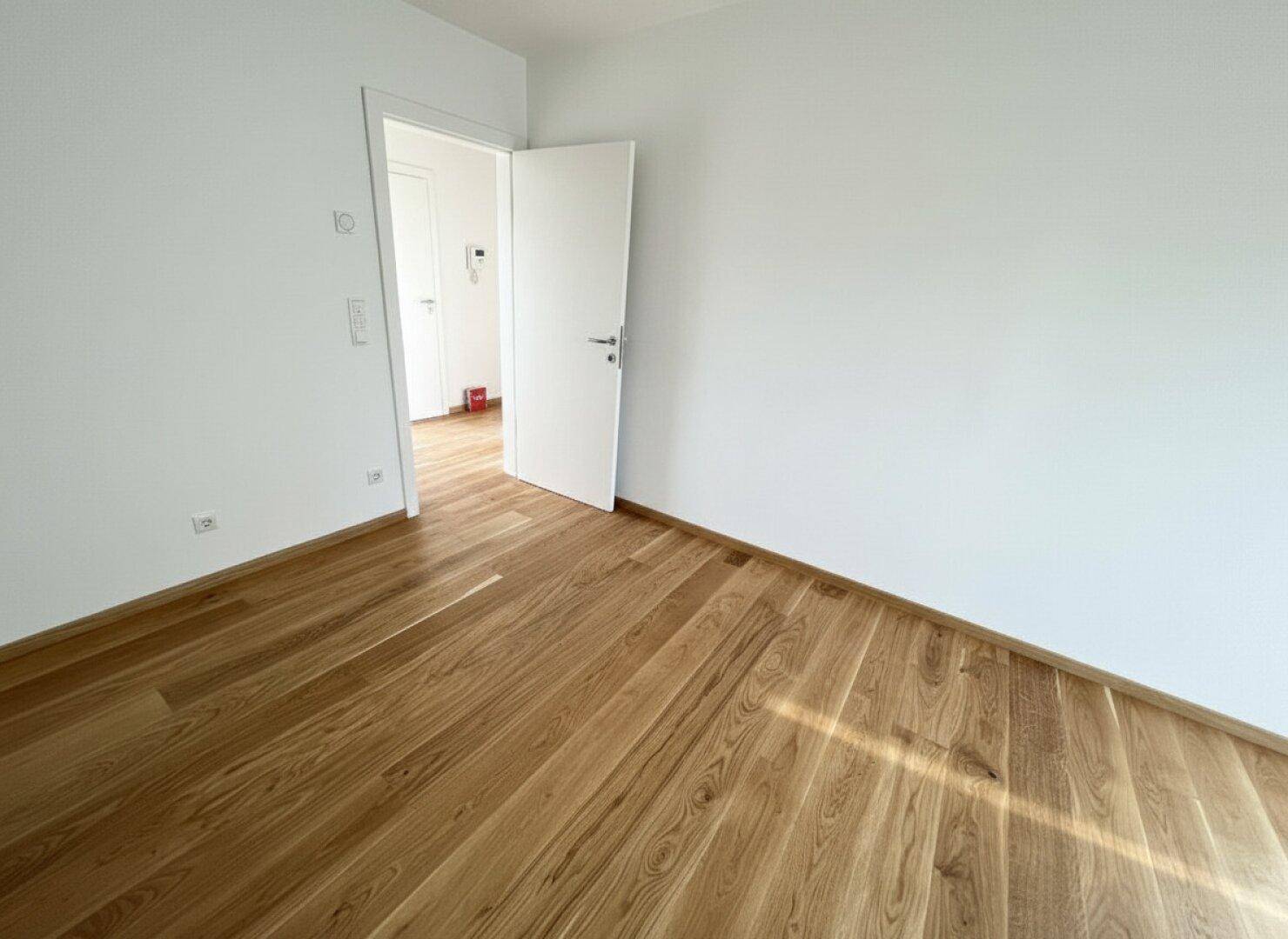 Leeres Zimmer mit Parkettboden und weiß gestrichenen Wänden, bereit zum Einzug.