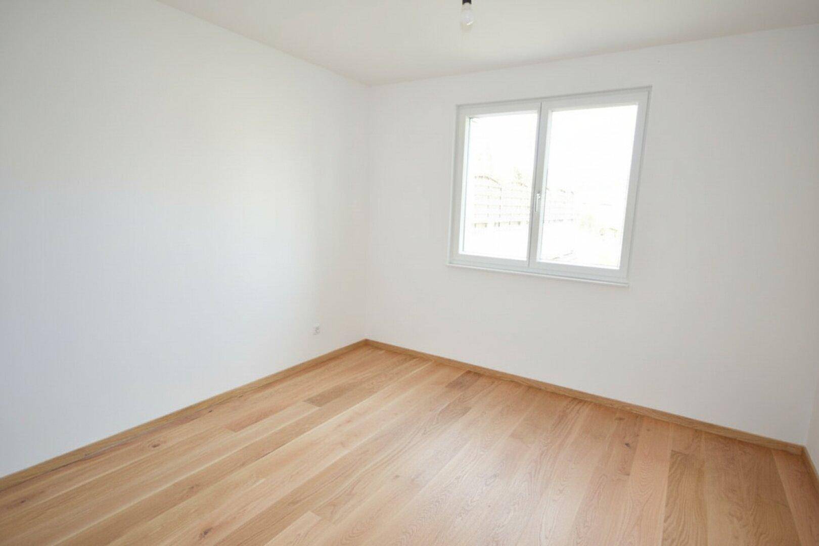 Helles Zimmer mit großem Fenster und Holzboden, bietet eine angenehme Wohnatmosphäre.