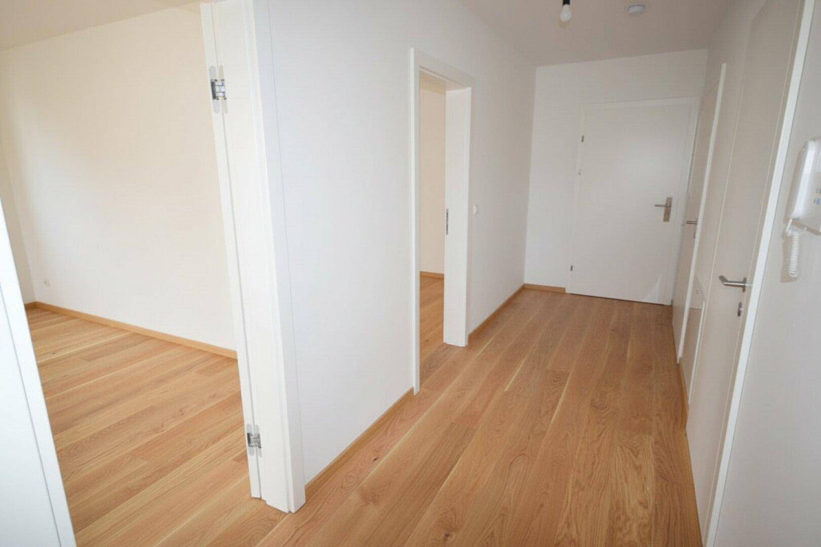 Heller Eingangsbereich mit Parkettboden, der zu den verschiedenen Räumen der Wohnung führt.